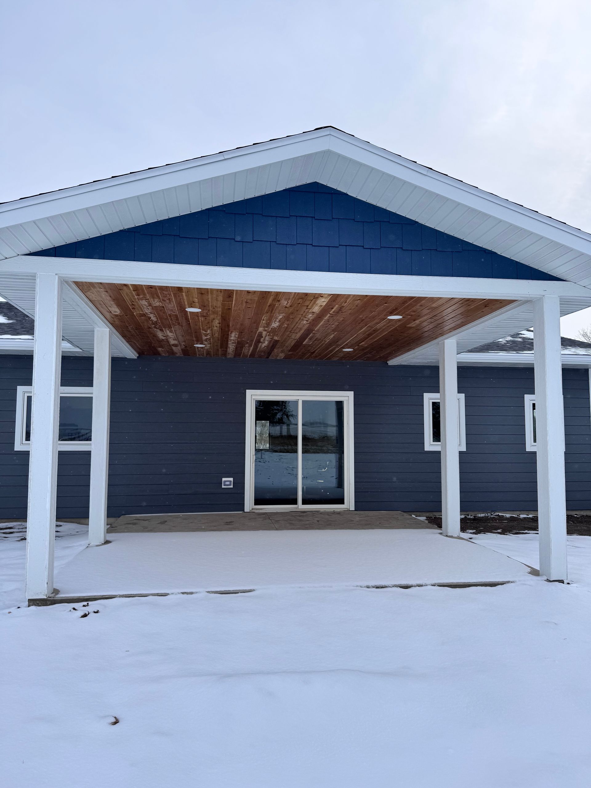 A snowy scene with a blue building, white porch, and sliding glass door.
