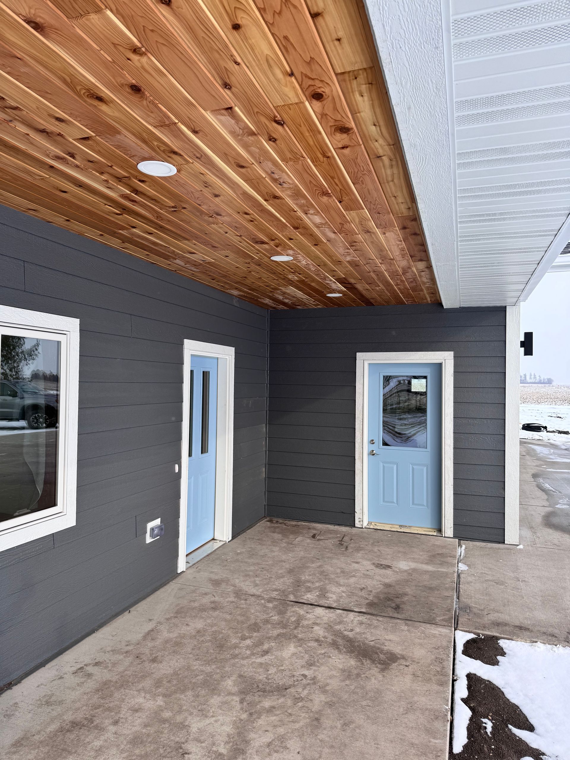 Covered porch with a wood ceiling, blue doors, and gray siding.