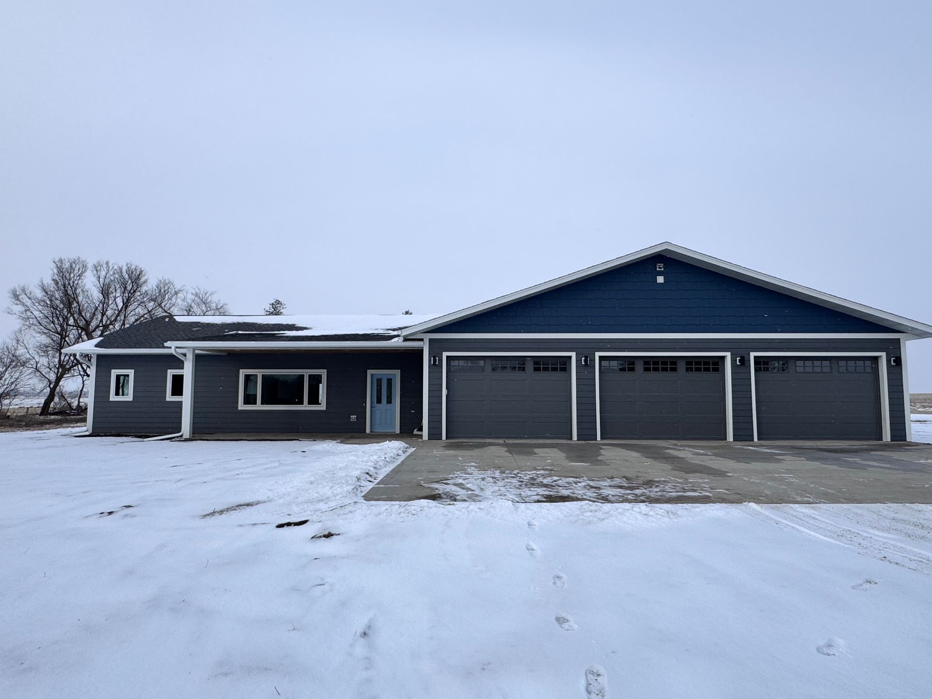 Gray house with blue trim and three-car garage on a snowy day.