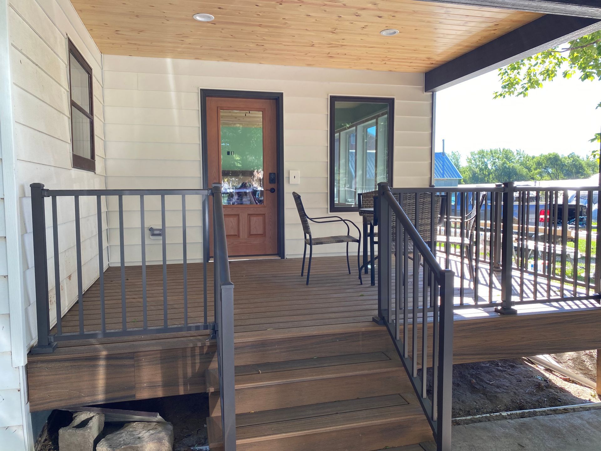 A porch with wooden steps, railing, and a door.  A table and chairs sit nearby.