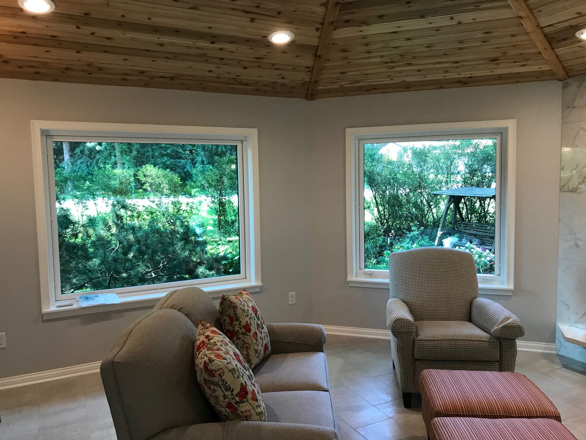 Living room with sofa, armchair, windows, and wood ceiling.