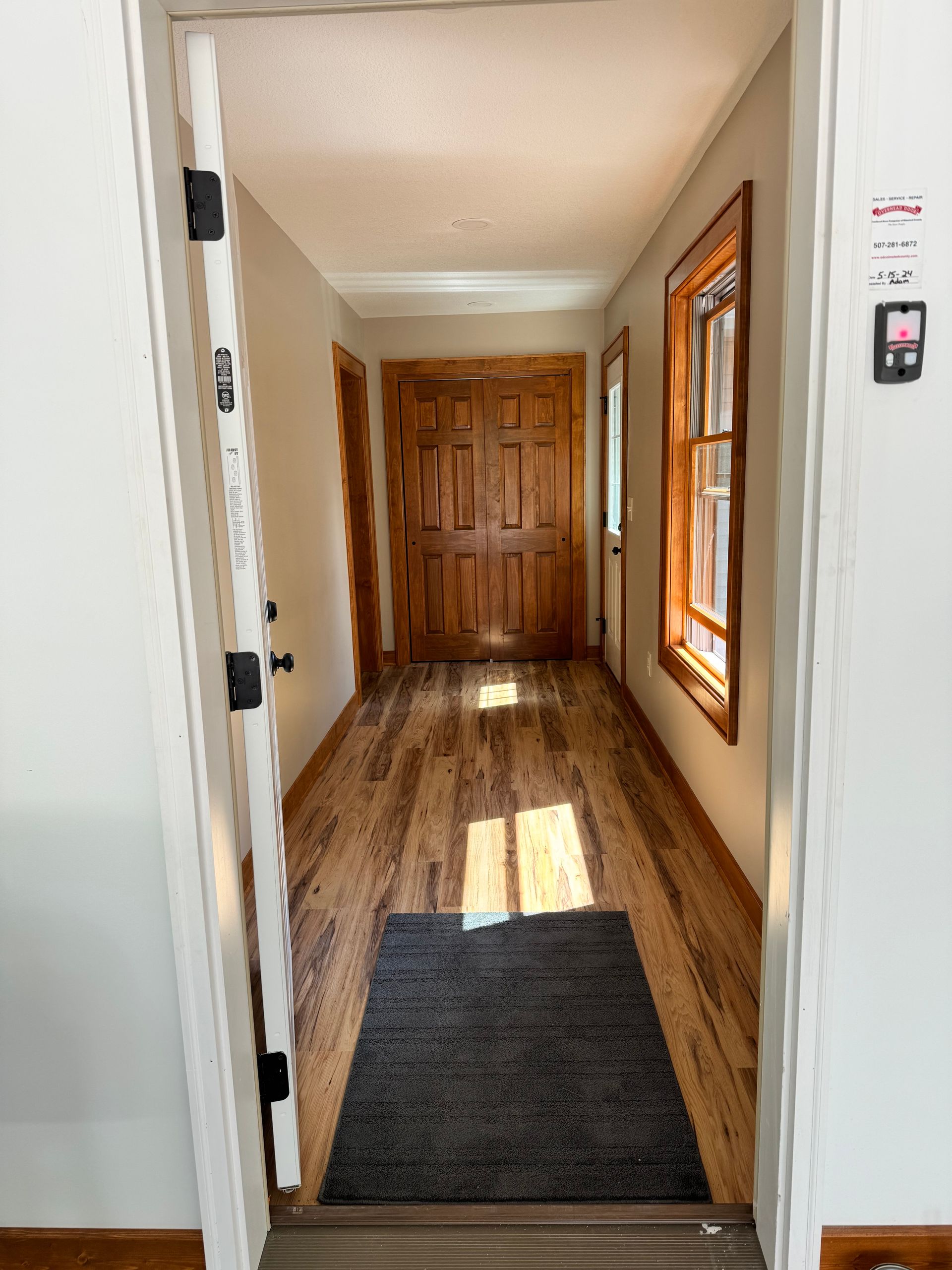 Hallway with wooden floors, a gray rug, and a brown wooden door at the end.