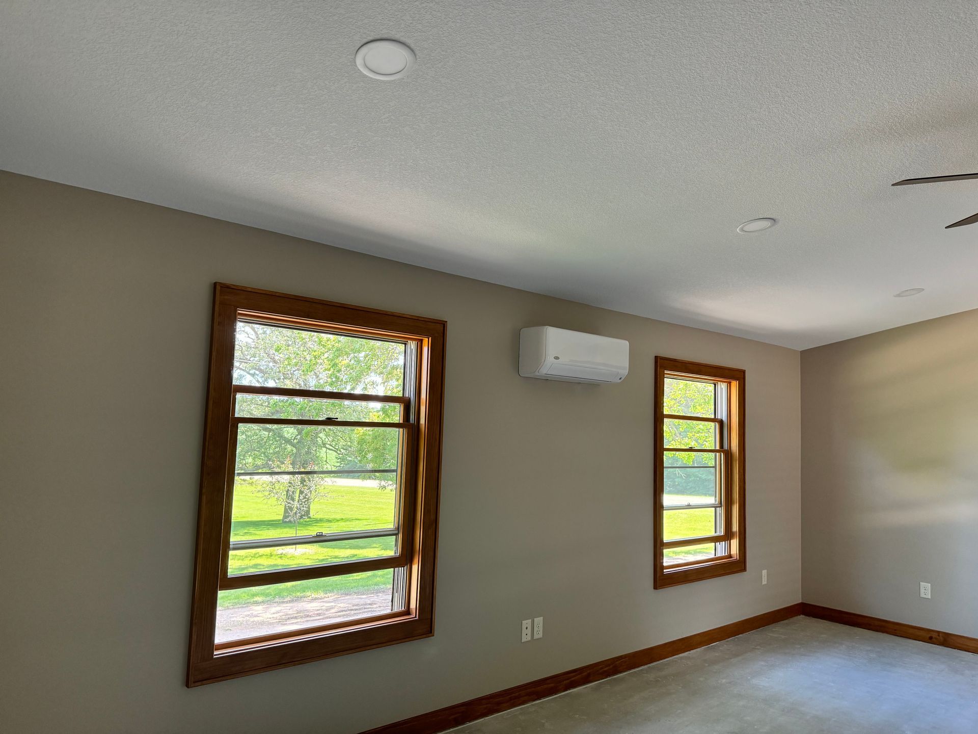 Bedroom with two windows framed in wood, tan walls, an AC unit, and recessed lighting.