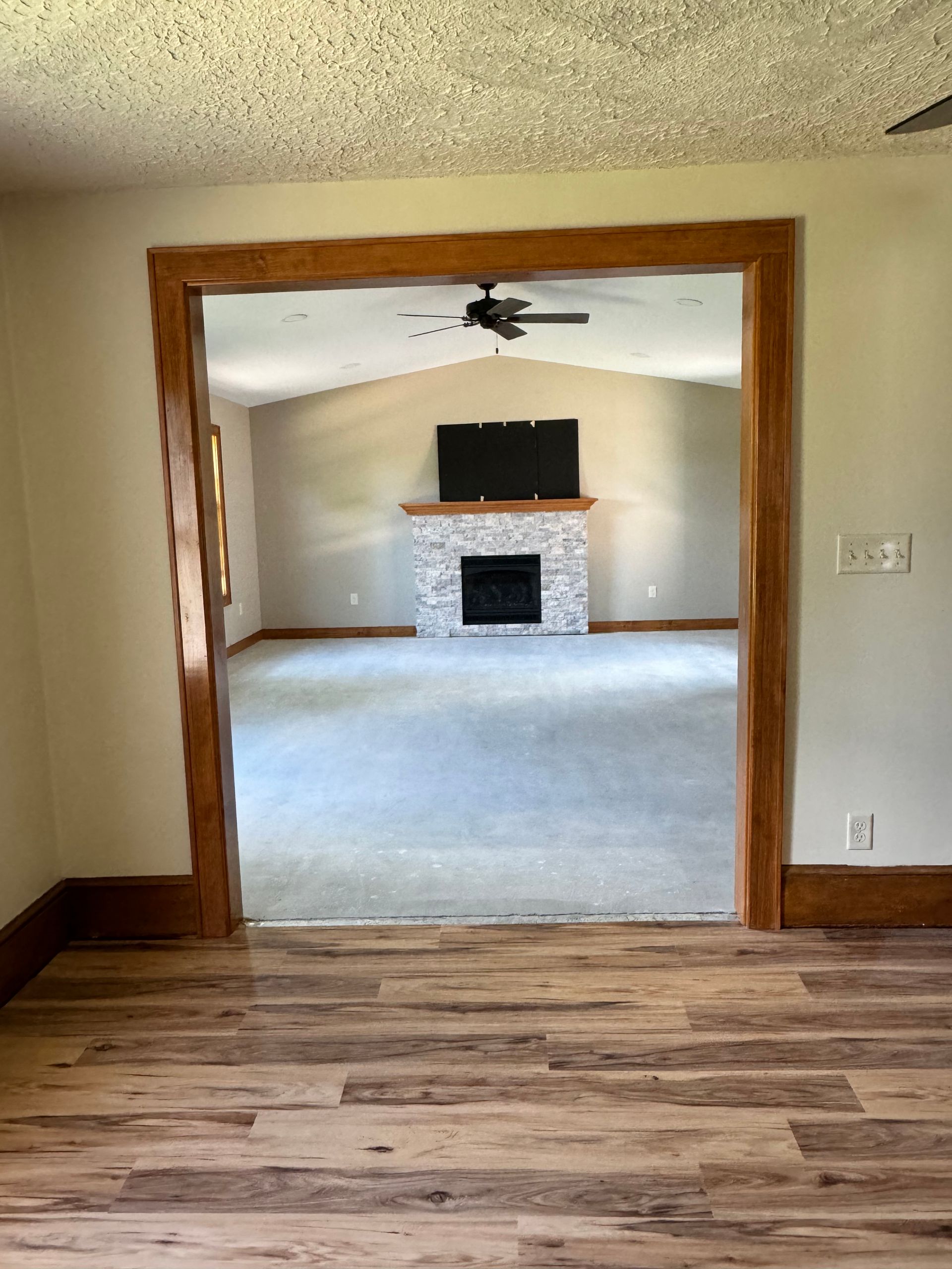 Room interior with wooden door frame. Gray carpet, fireplace, and TV.
