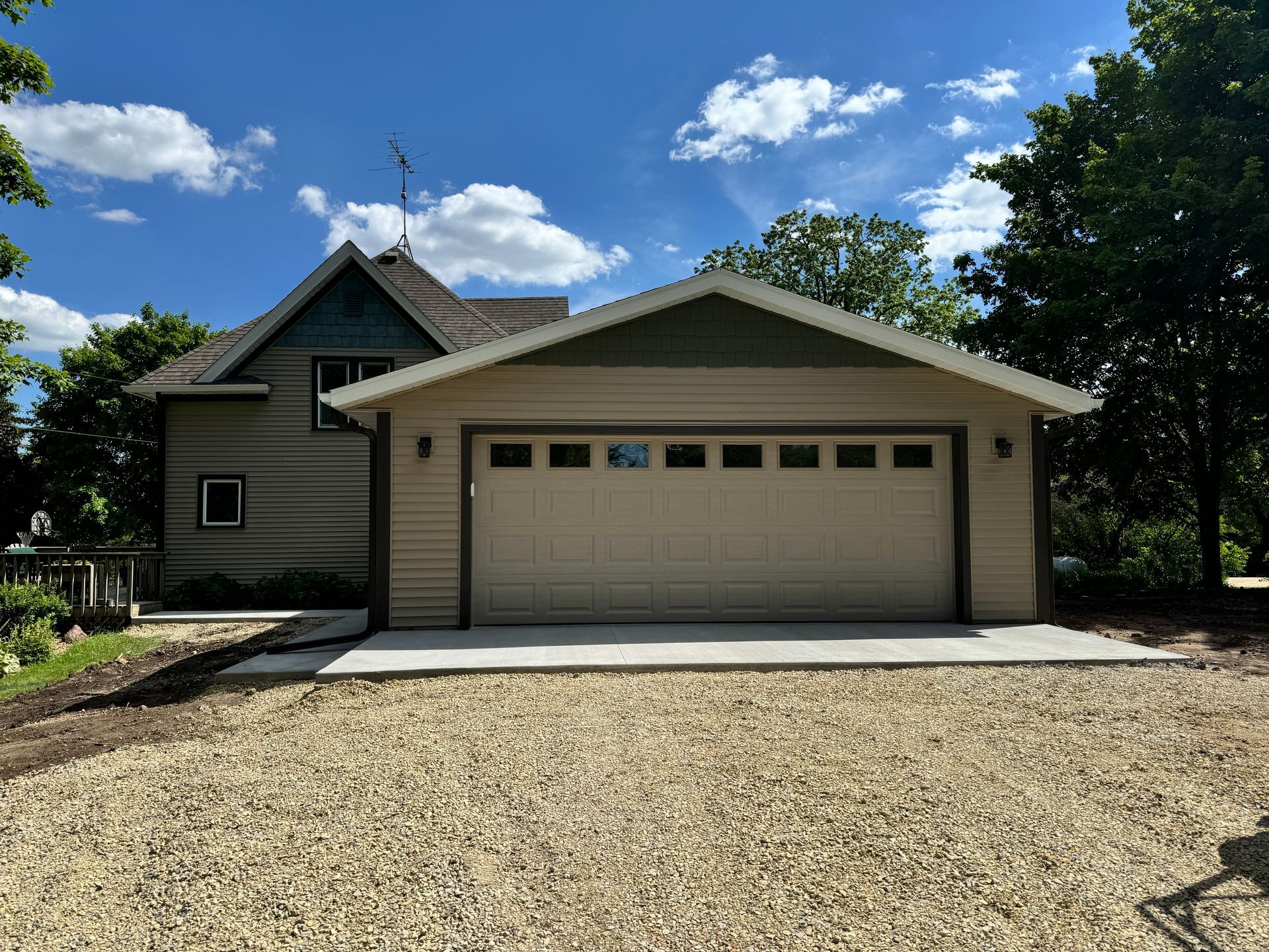 Tan garage with a driveway, attached to a two-story house on a sunny day.
