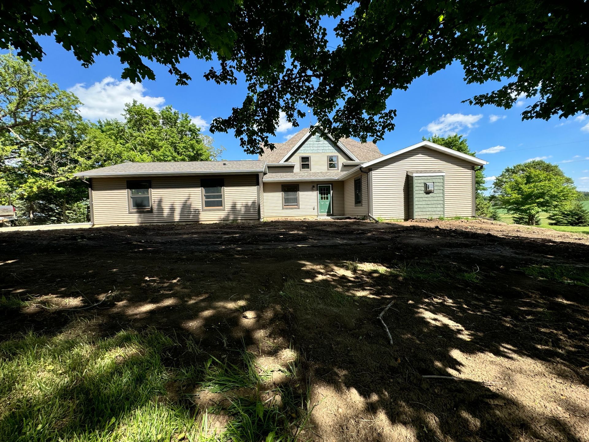 Old farmhouse with wooden siding on a sunny day; blue sky, trees in the background.