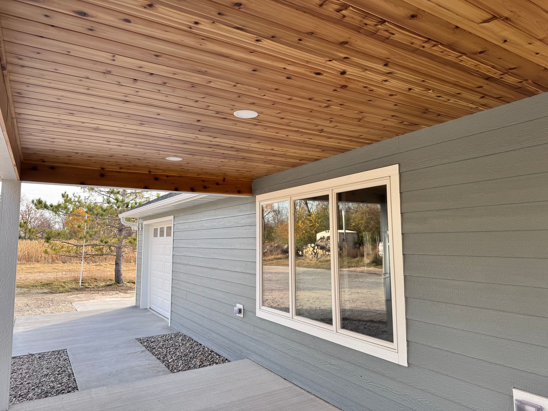 Covered porch with wood ceiling, blue-gray siding, white-framed windows, and a garage.