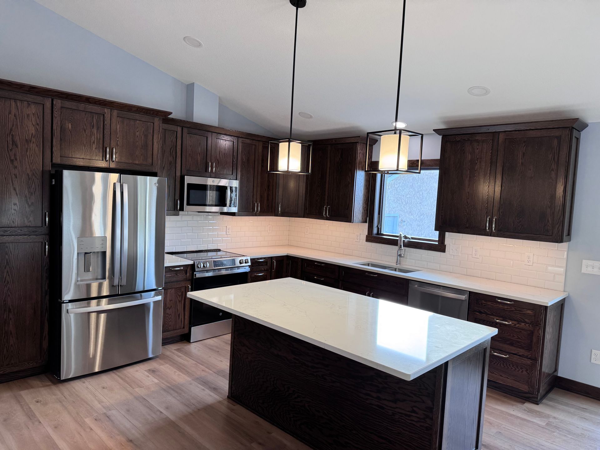 Dark wood kitchen with stainless steel appliances, white countertops, and a central island.