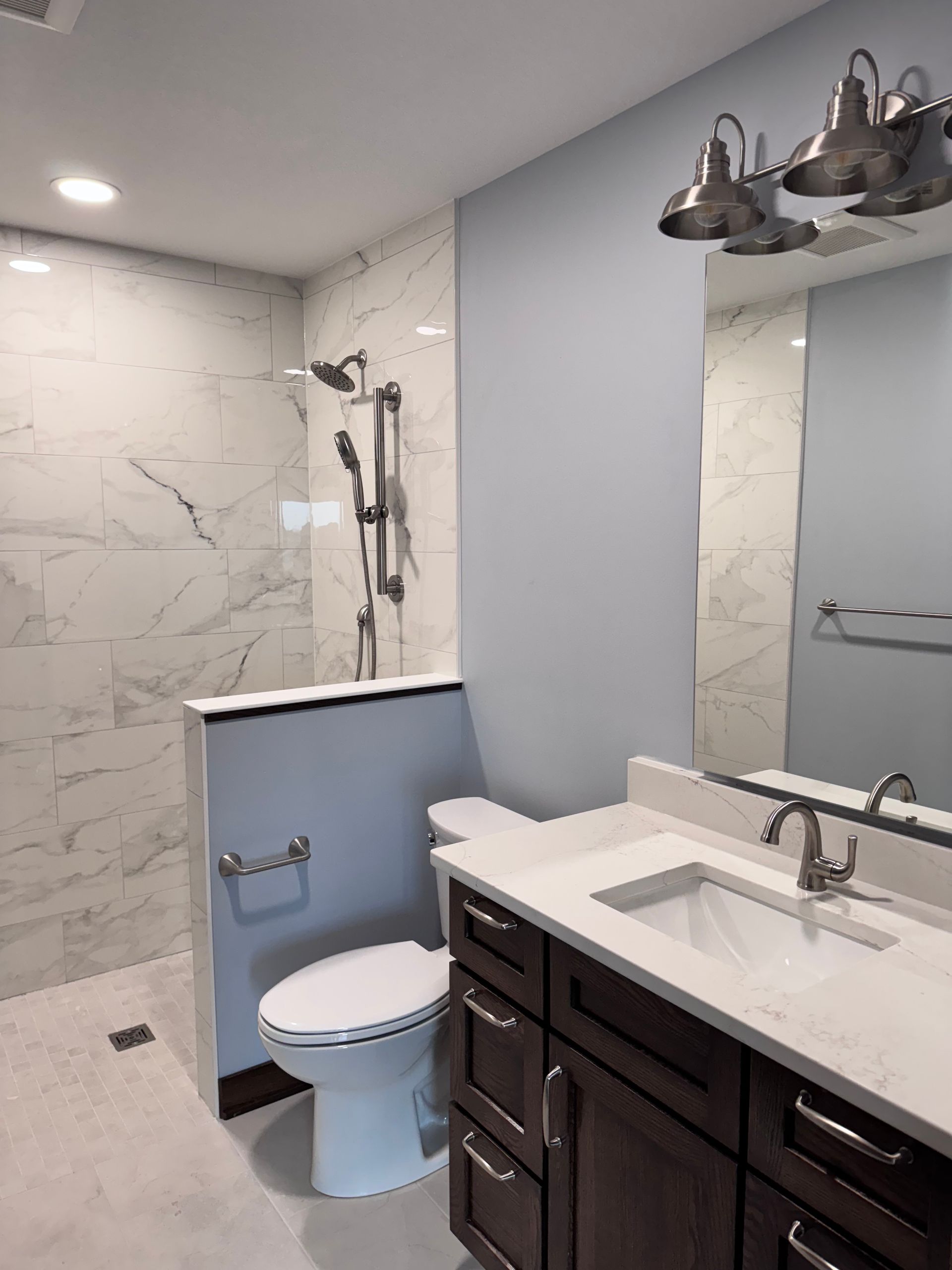 Bathroom with marble shower, blue wall, dark vanity, and silver fixtures.