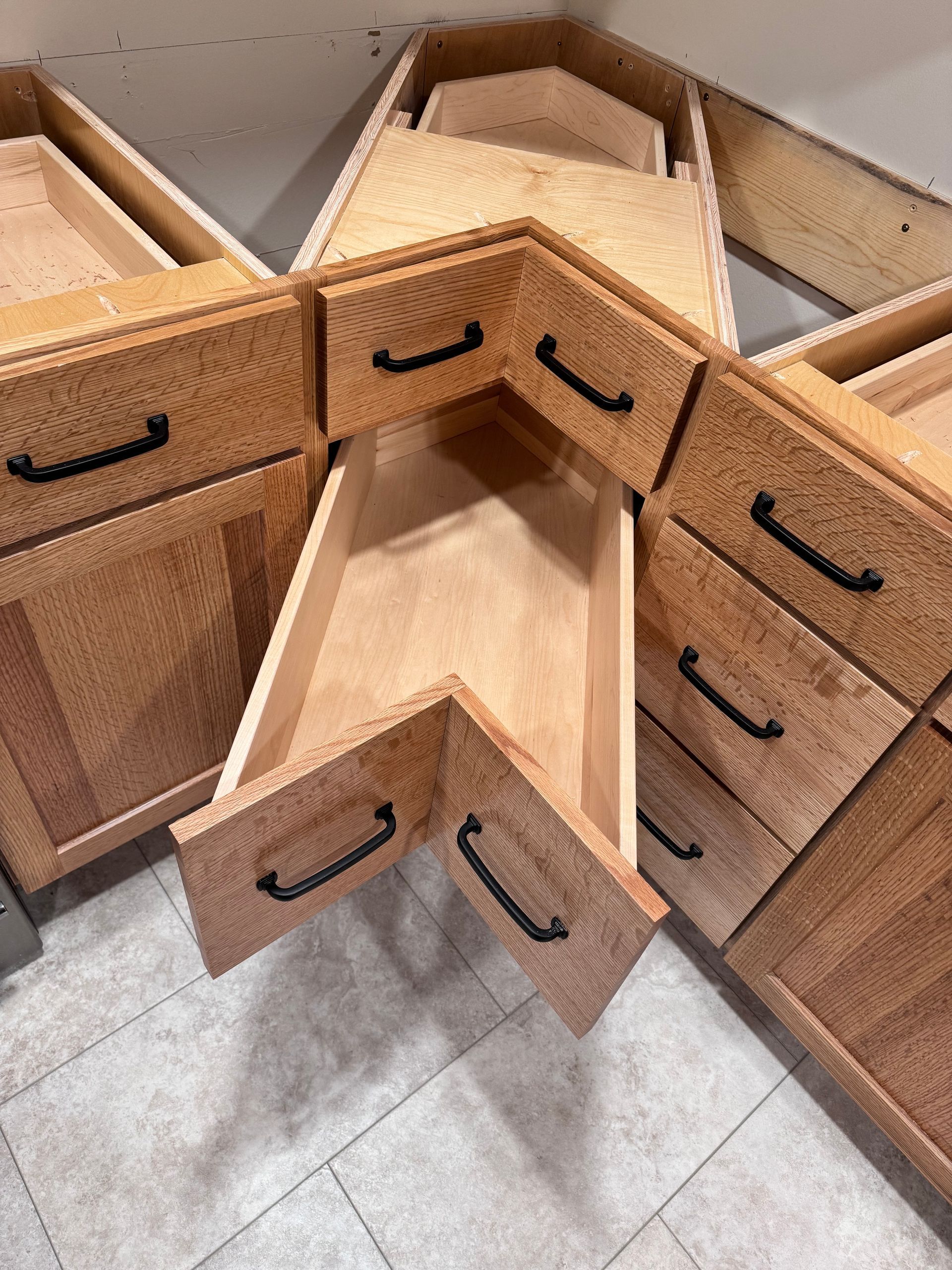 Light-wood kitchen cabinets with black handles, featuring a corner drawer open.