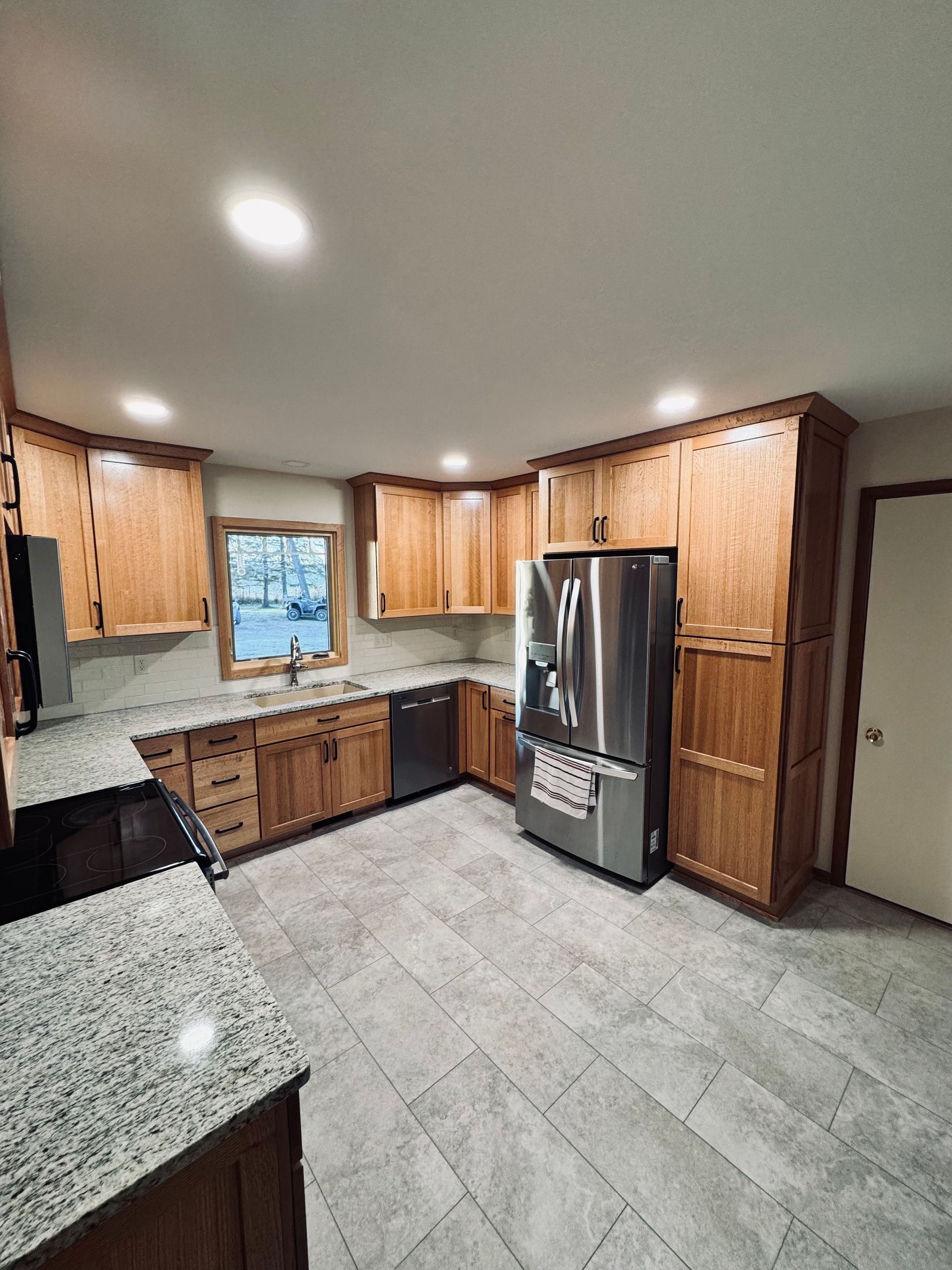 A kitchen with wood cabinets, stainless steel appliances, granite countertops, and tile flooring.