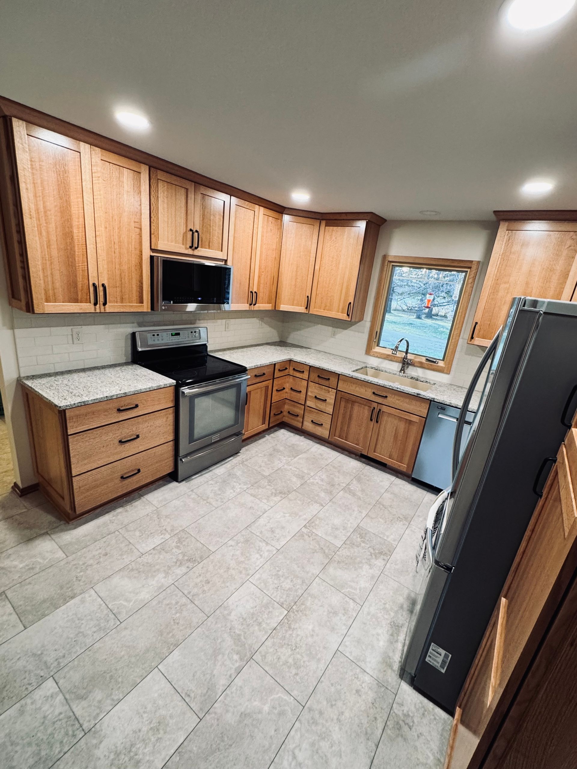 A kitchen with light wood cabinets, stainless steel appliances, and light gray tile flooring.