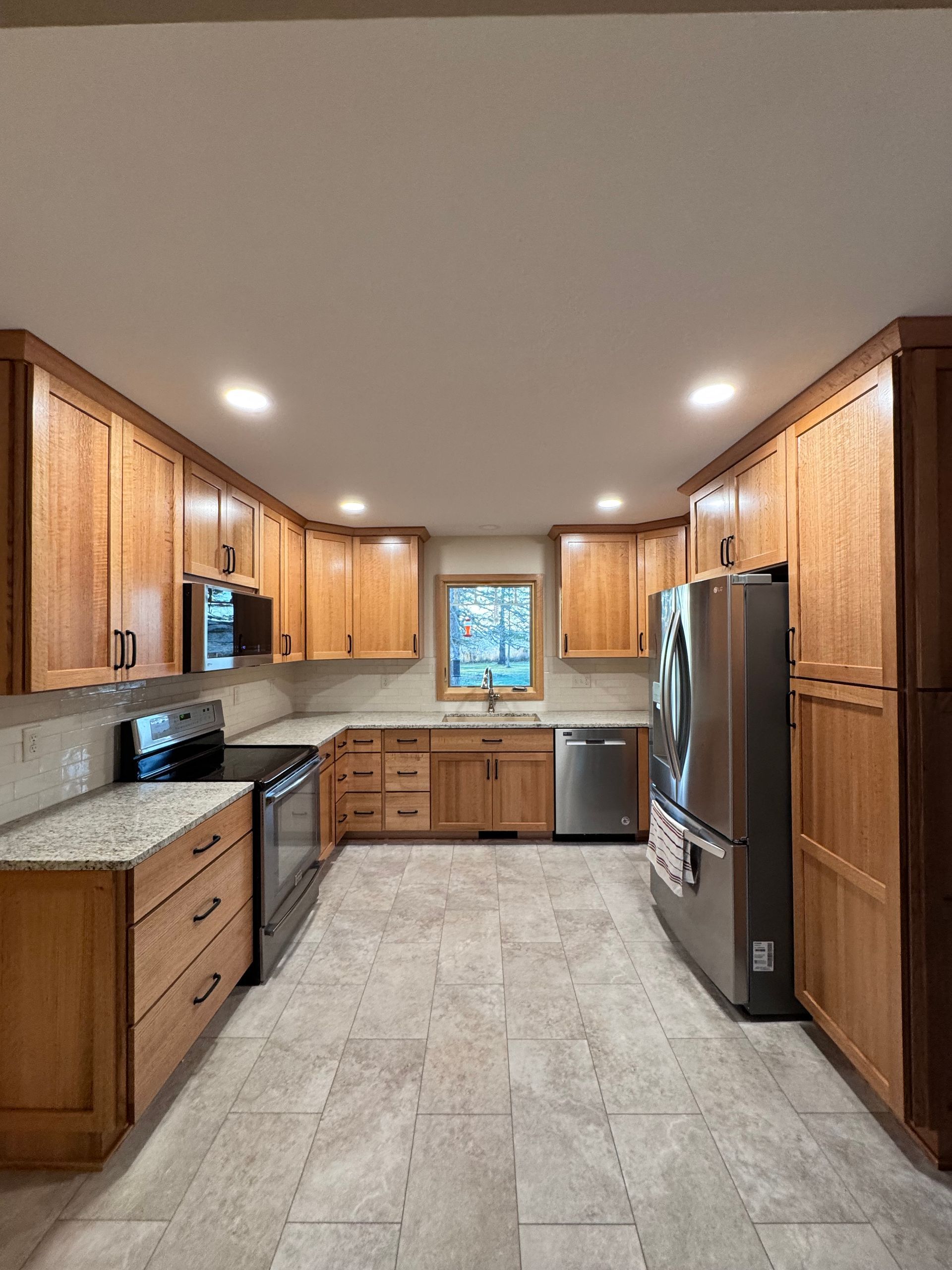 Kitchen with light wood cabinets, stainless steel appliances, and gray tile flooring.