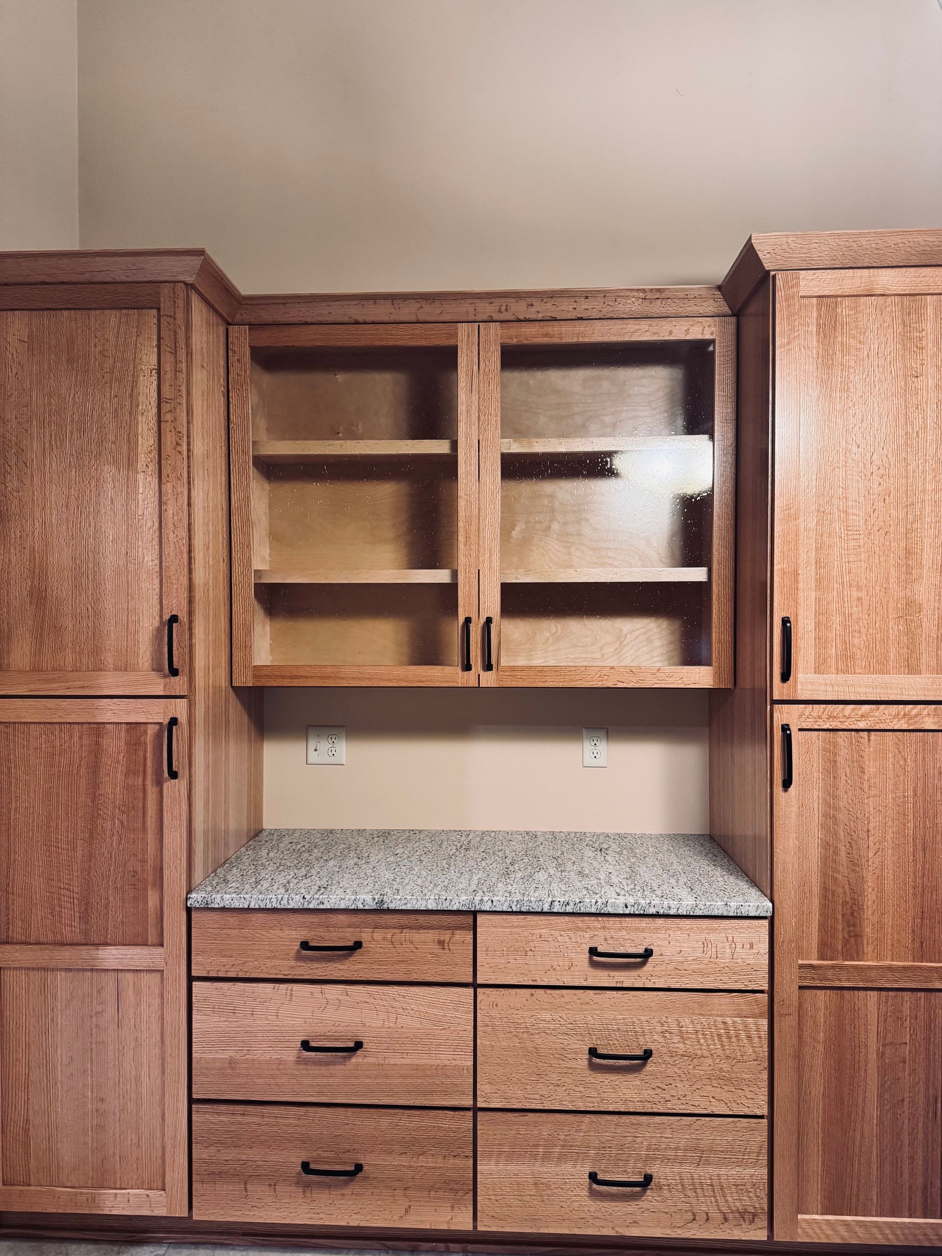 Wooden kitchen cabinets with a granite countertop, drawers, and glass-door upper cabinets.
