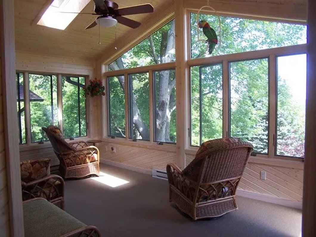 Sunroom with wicker chairs, large windows, and a view of trees.