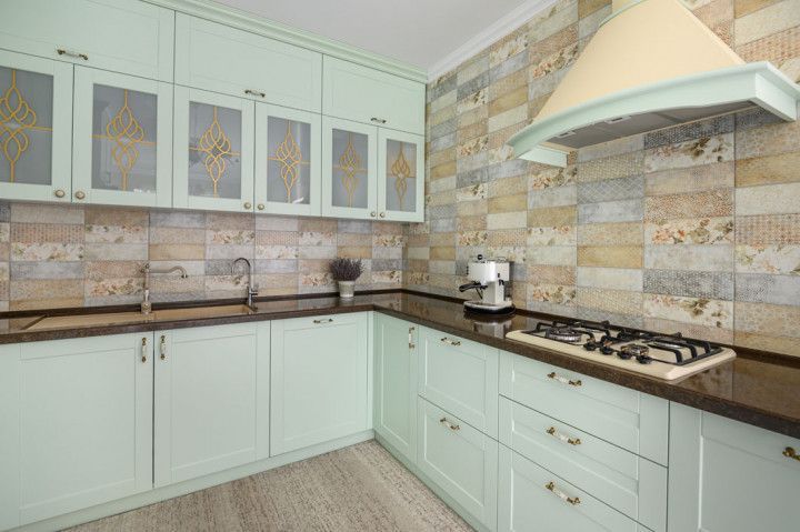 Mint-colored kitchen cabinets with patterned backsplash, stovetop, and range hood.