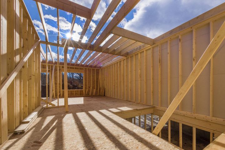 Interior view of a building under construction, wooden framework, blue sky visible.