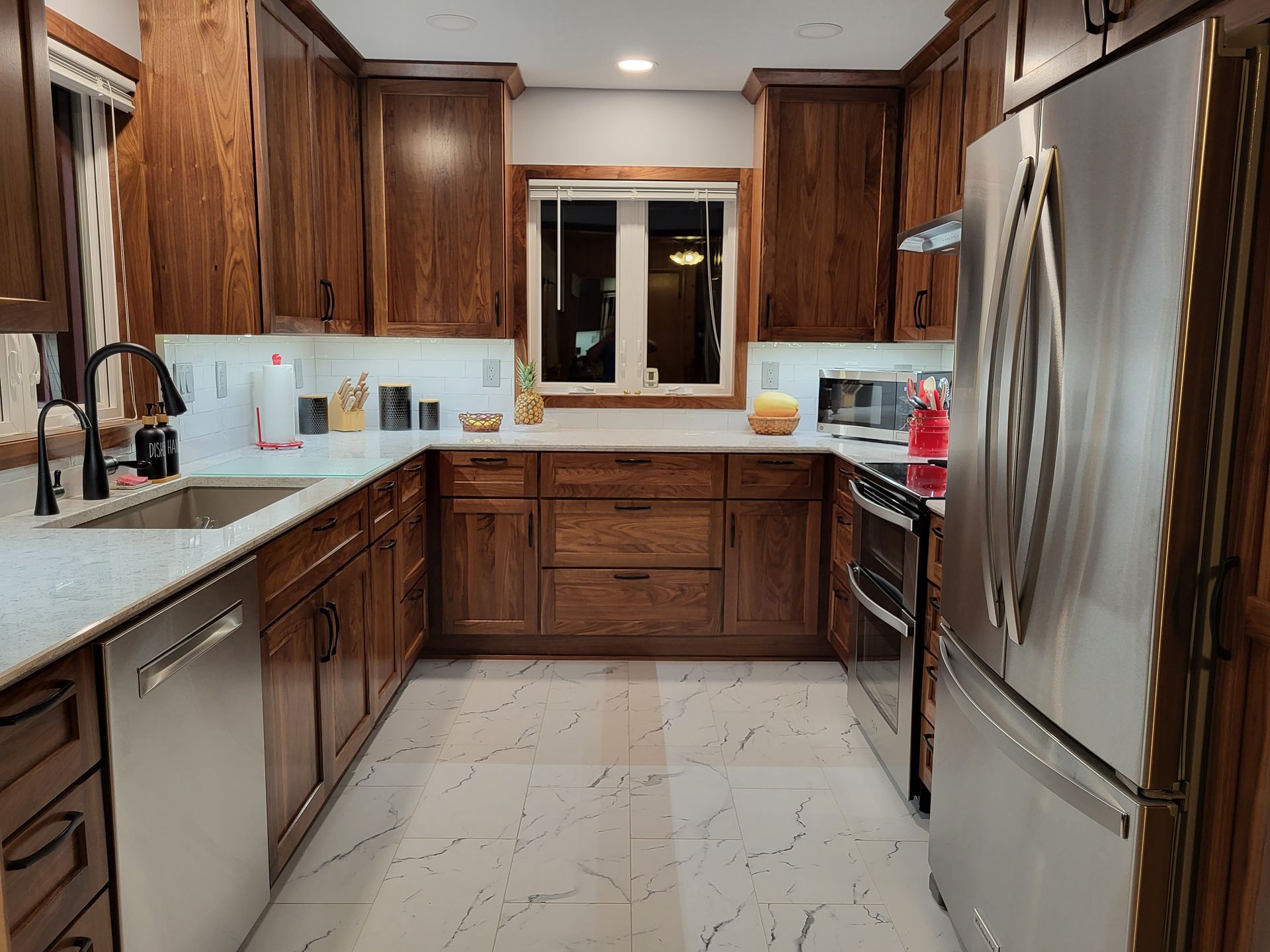 U-shaped kitchen with brown cabinets, stainless steel appliances, white countertops, and a window.