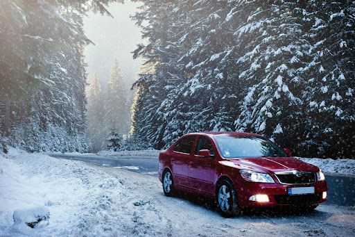 Red car driving through a snowy forested area. 