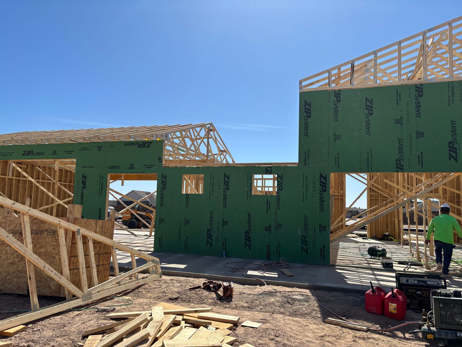 Partially built house with green sheathing and wooden framing at a construction site under a clear blue sky