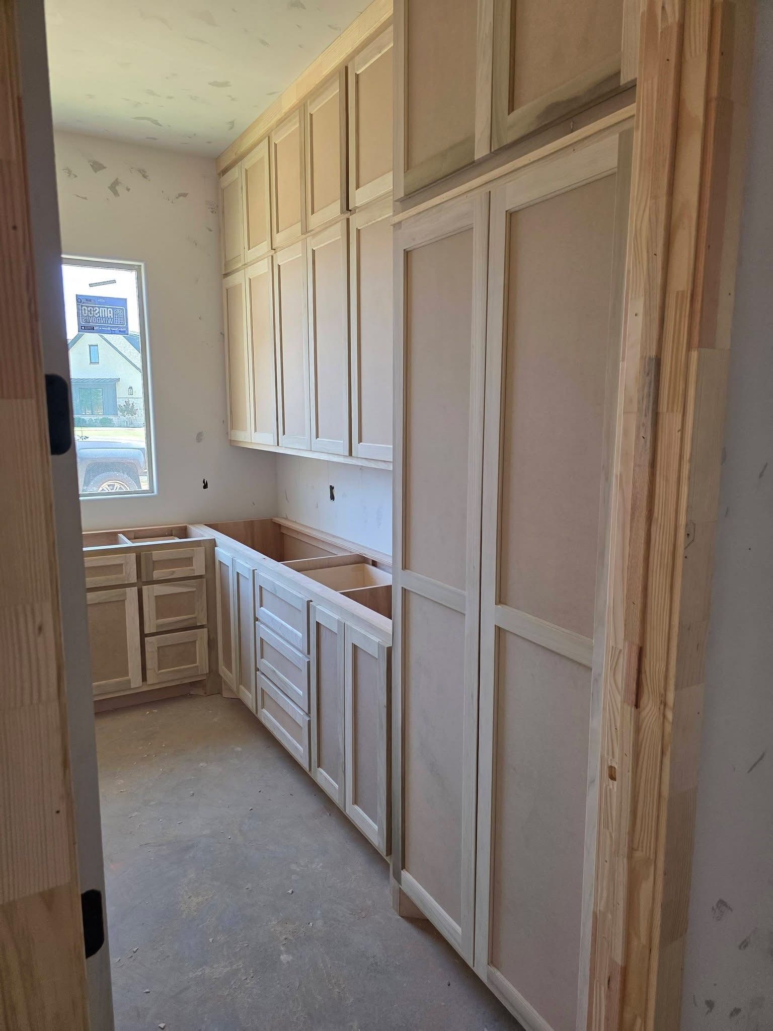 Narrow kitchen with unfinished white cabinets and drawers along both sides of a hallway-like space.