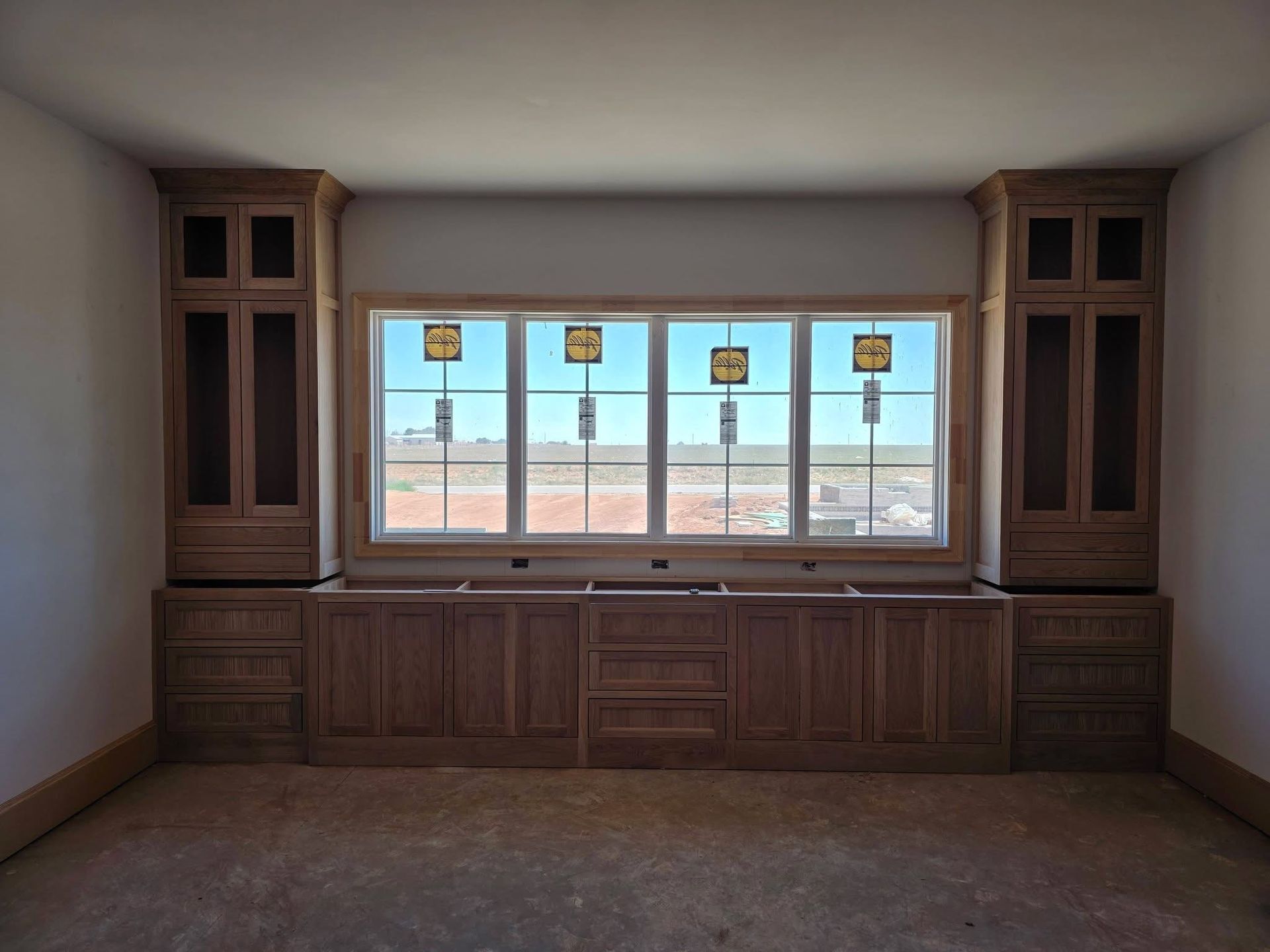 Built-in wood cabinets and drawers beneath a large window in an empty room