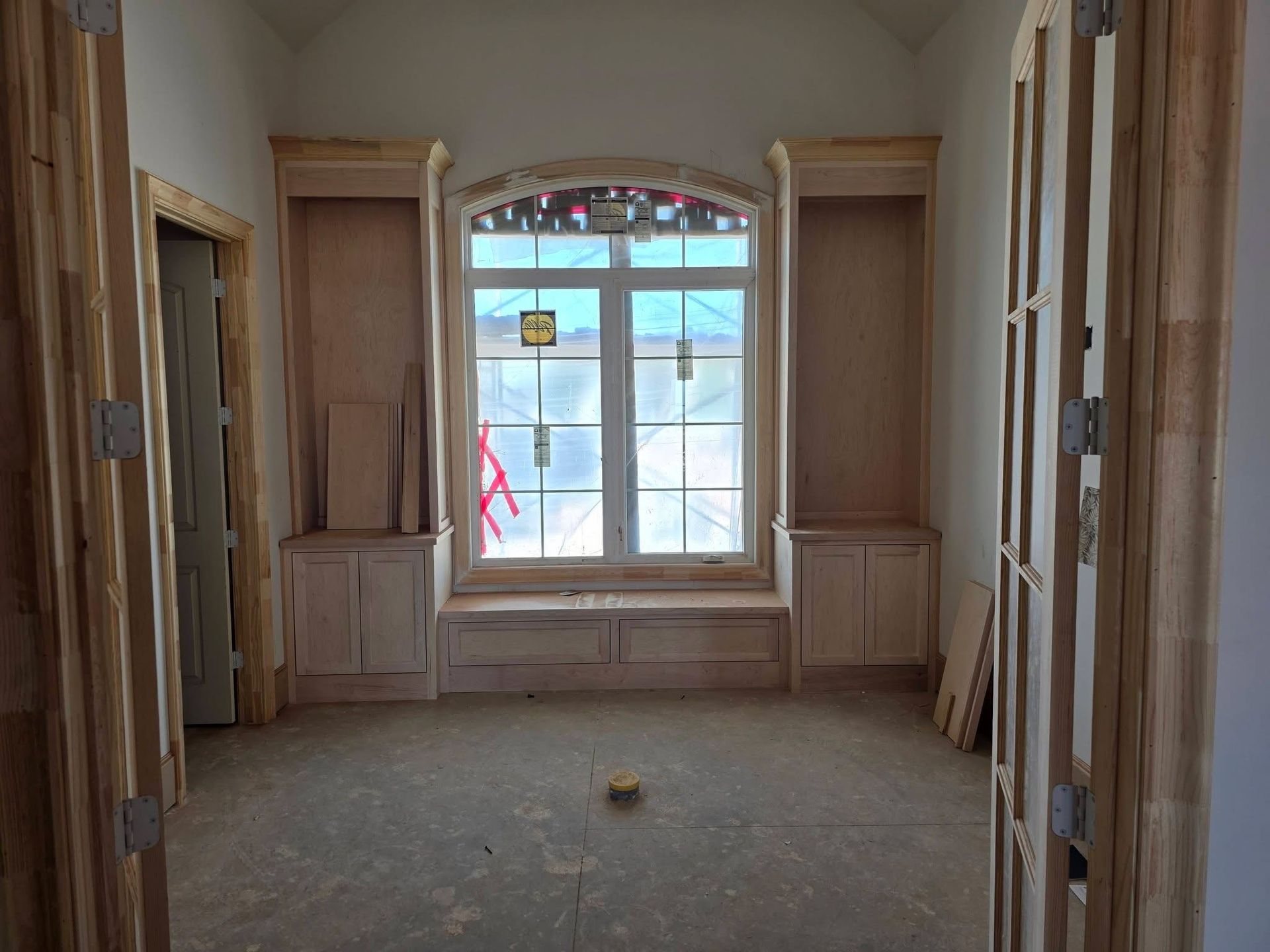 Unfinished room with built-in wood cabinets and a large window, lit by daylight.