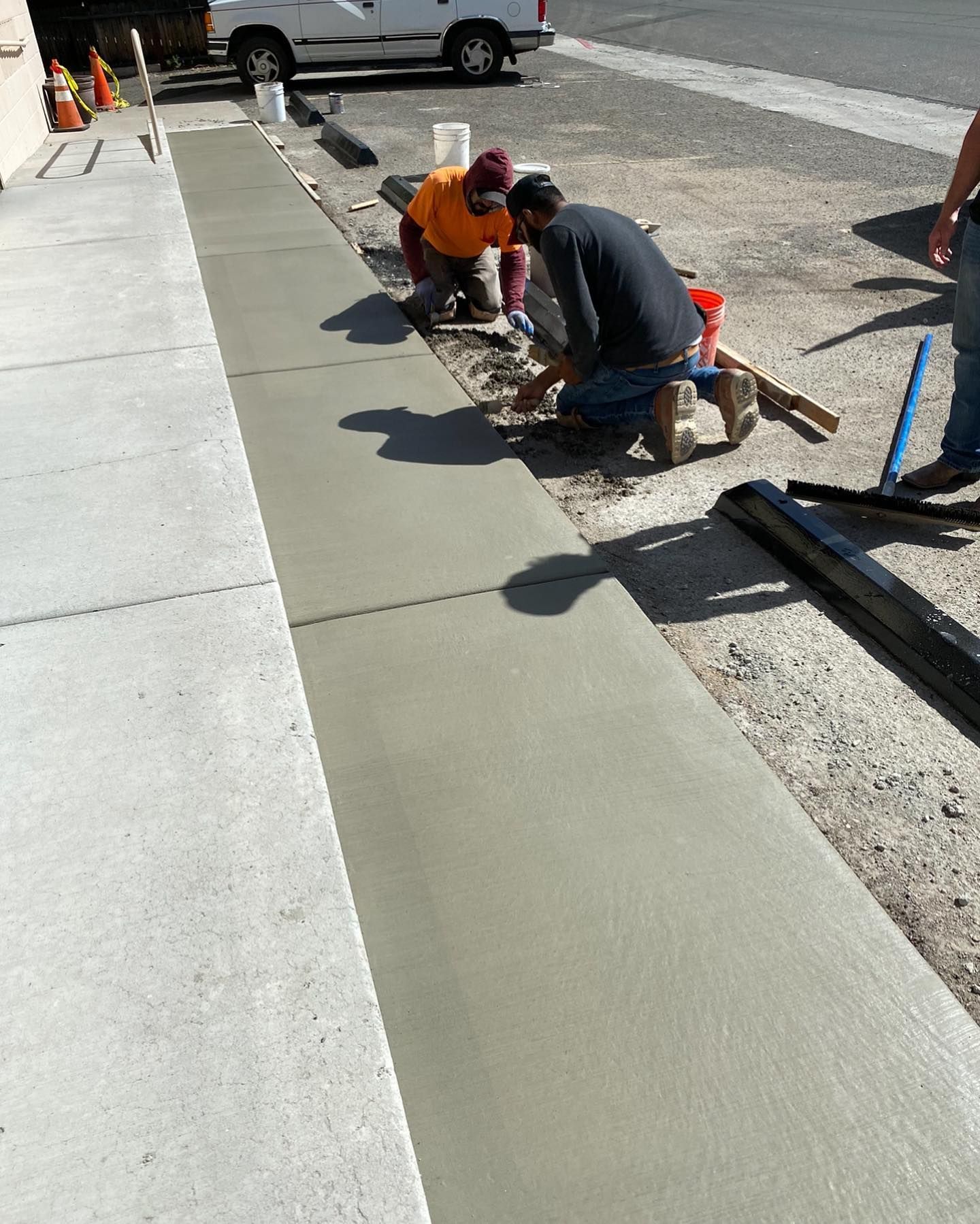 Two workers finish a fresh concrete sidewalk outdoors on a sunny day.