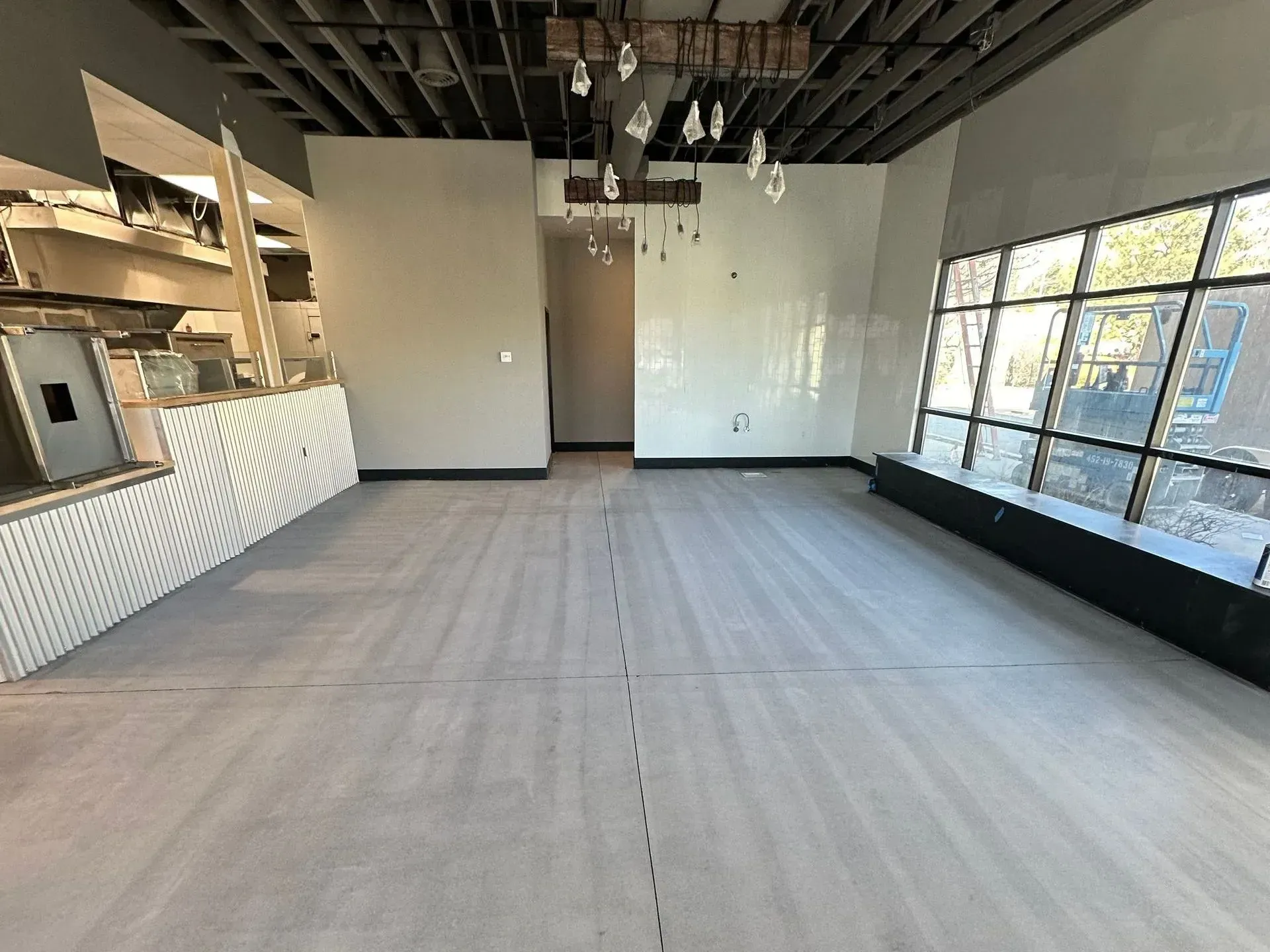 Empty interior of a commercial space with grey flooring, white walls, a service counter, and a large windowed wall.