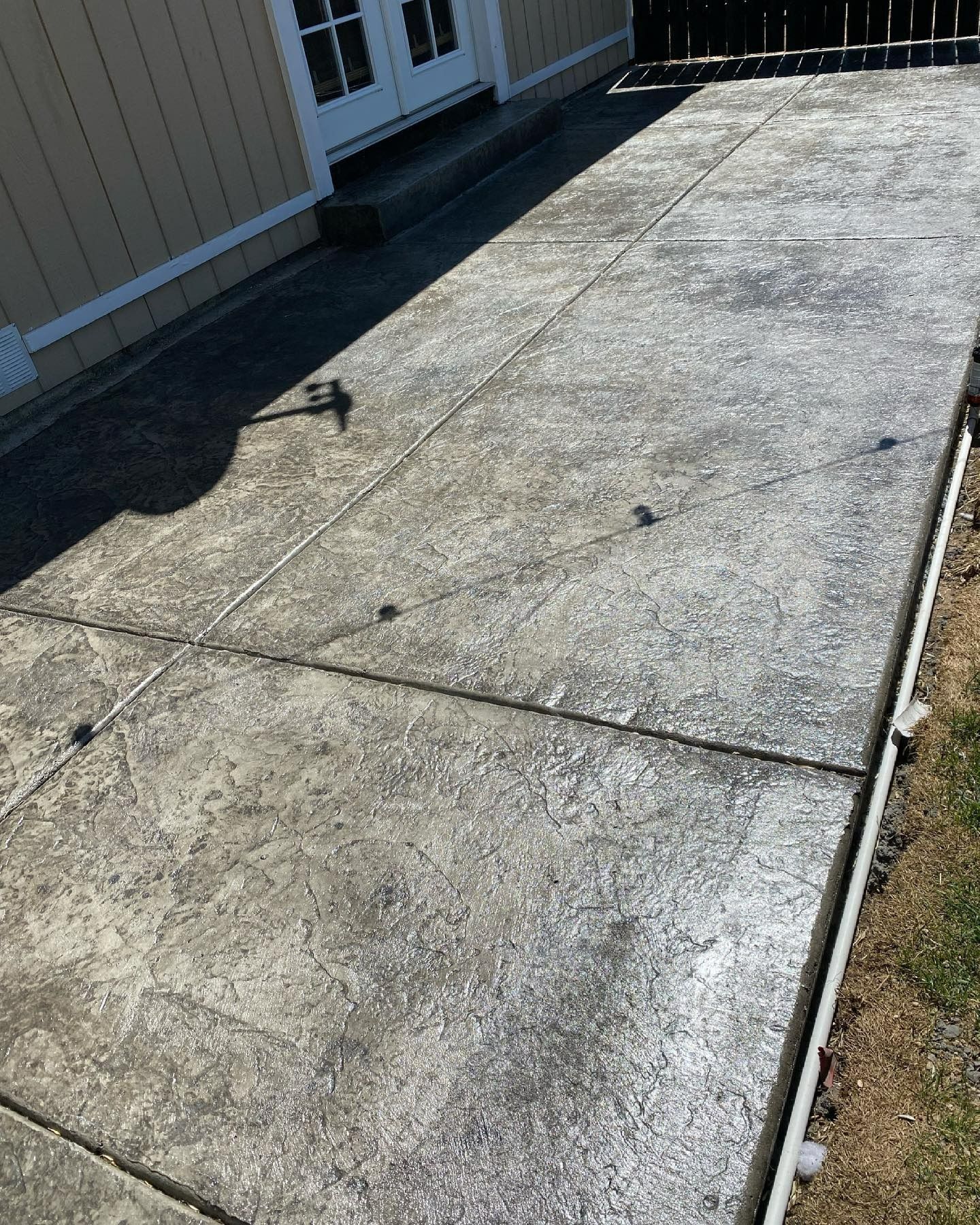 A weathered, stamped concrete patio extends from the side of a light-colored house with a glass-paneled door.