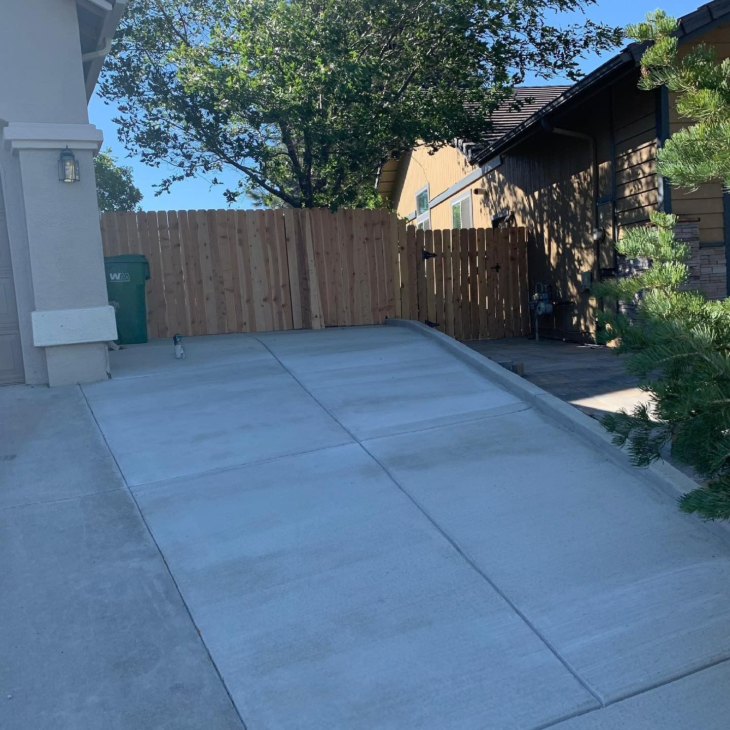 A concrete driveway ramp leading up to a wooden fence gate situated between two house structures on a sunny day.
