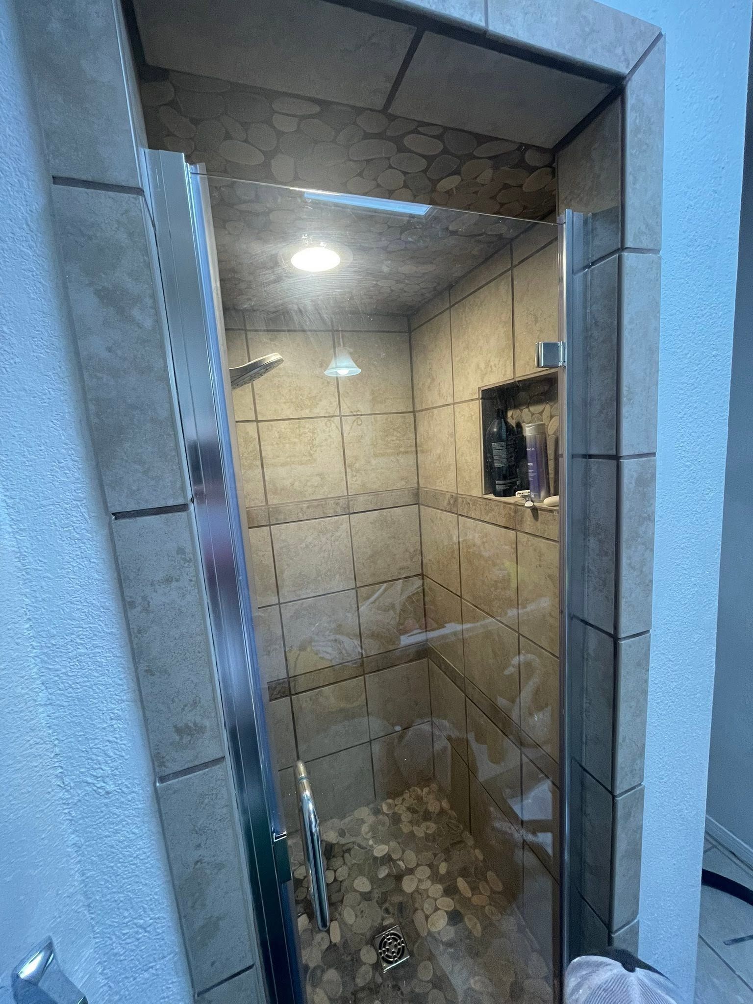 Small tiled shower stall with glass door, lit by a ceiling light.