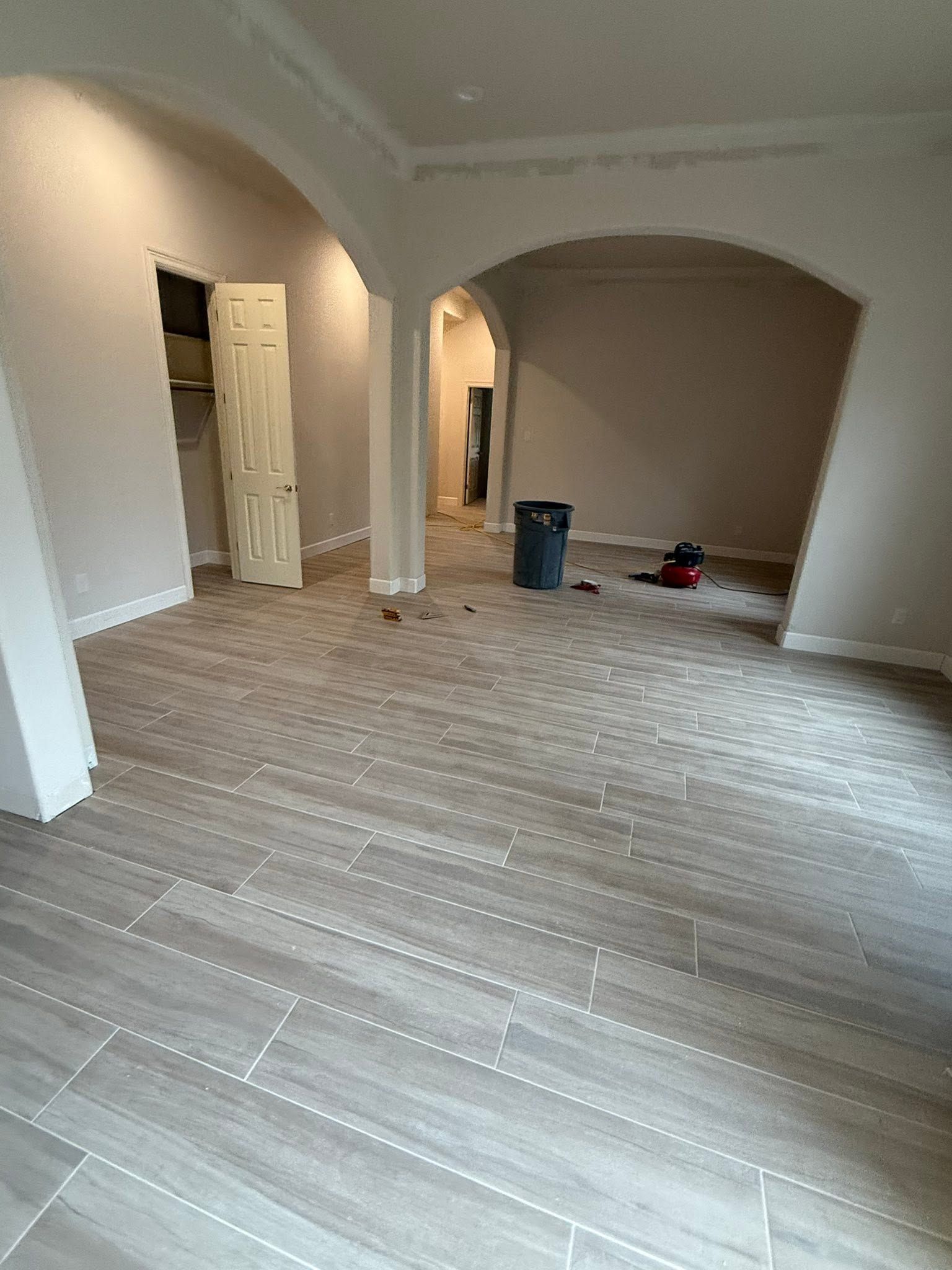 Empty unfinished room with arched doorways, tiled floor, and a few construction items on the right