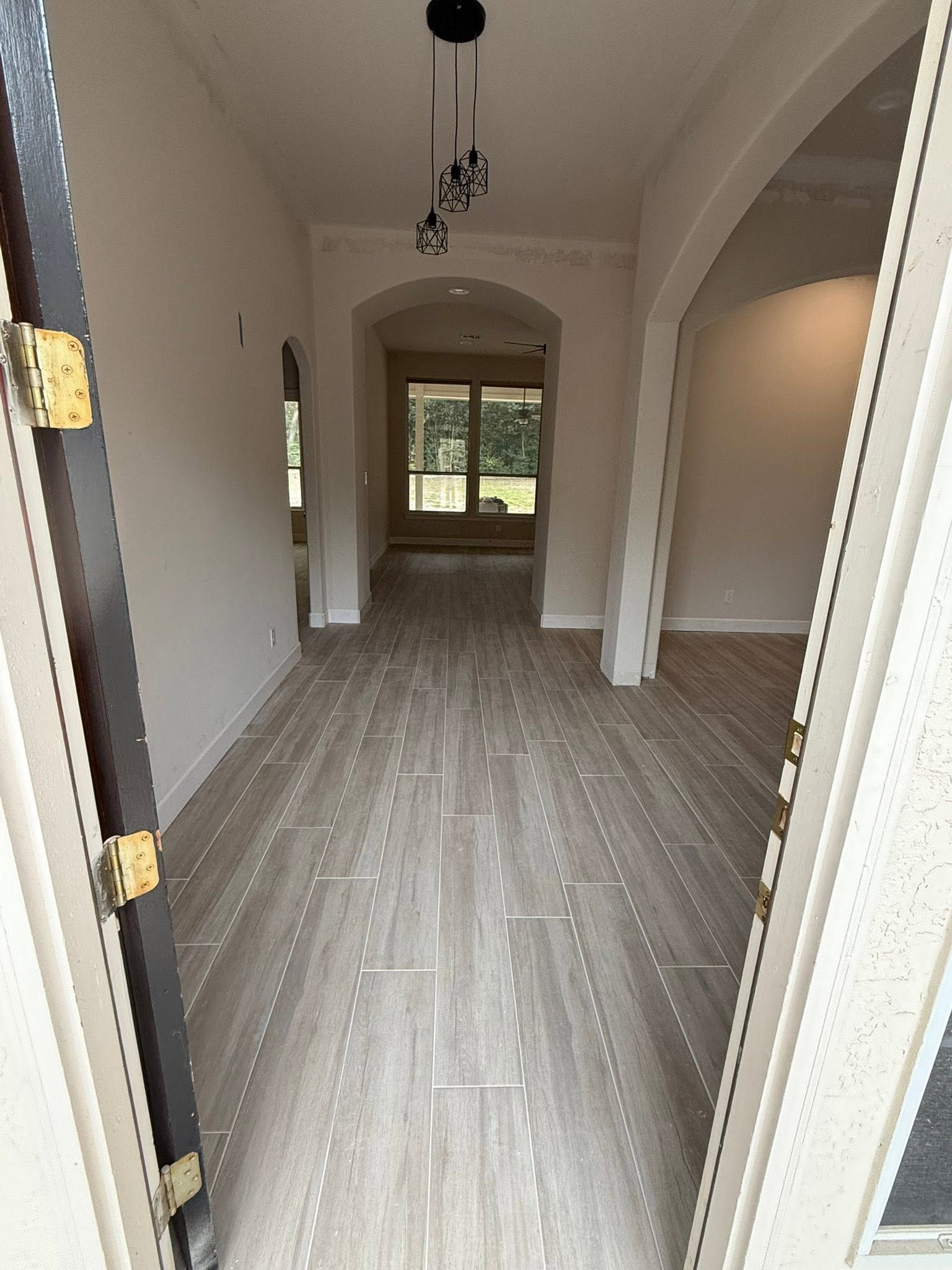 Empty narrow hallway with light wood floors, white walls, and a window at the far end.