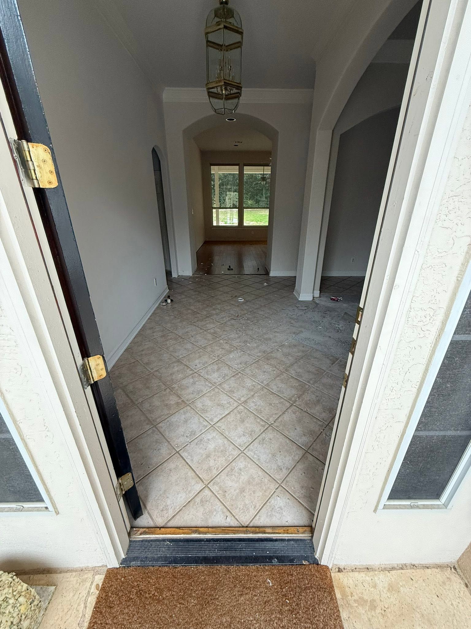 Open front doorway to a tiled hallway with white walls and a window at the far end.