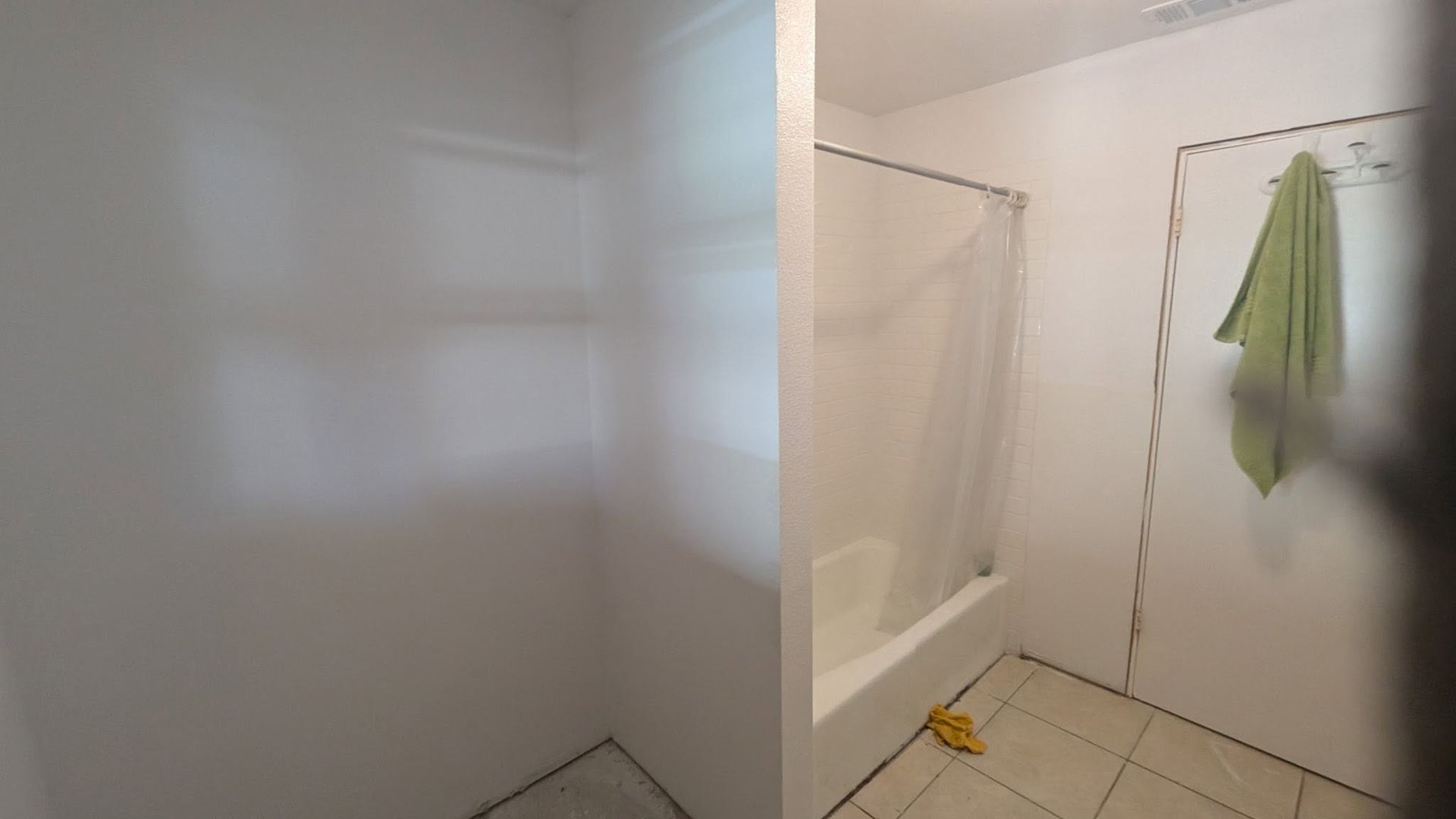 Small bathroom with white walls, a bathtub, tiled floor, and a green towel hanging on the door.