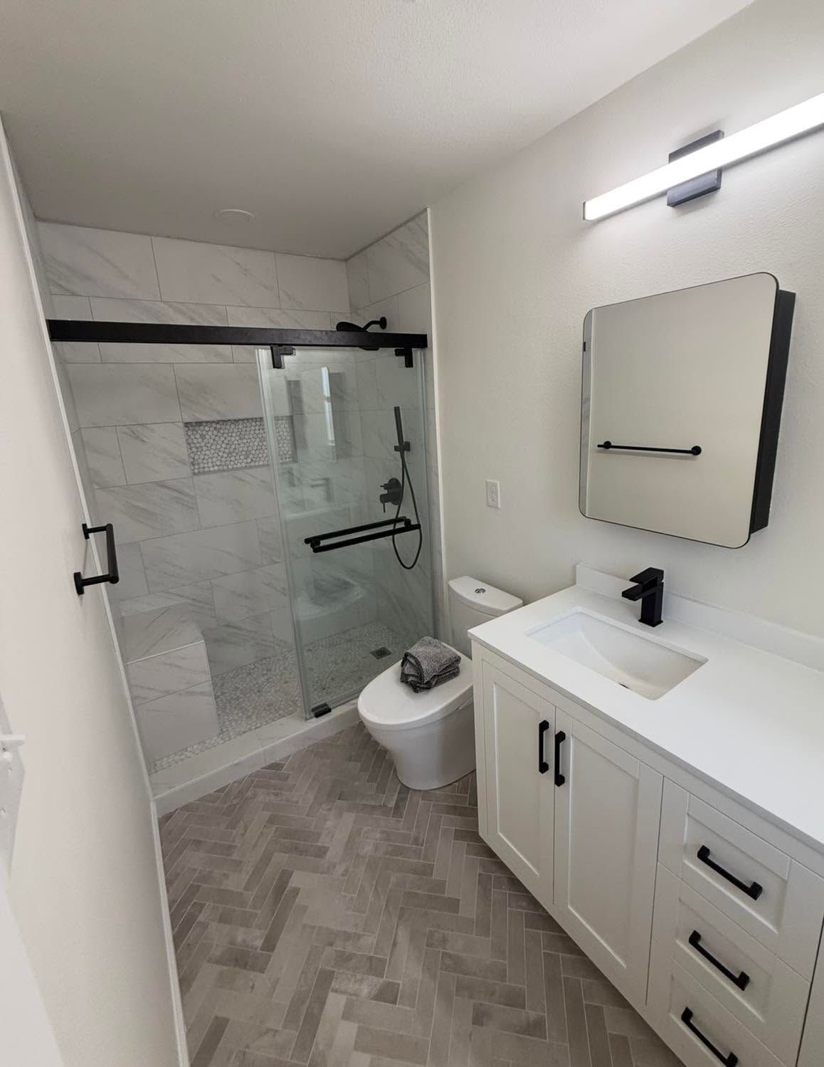Modern white bathroom with glass shower, toilet, and vanity with mirror light.