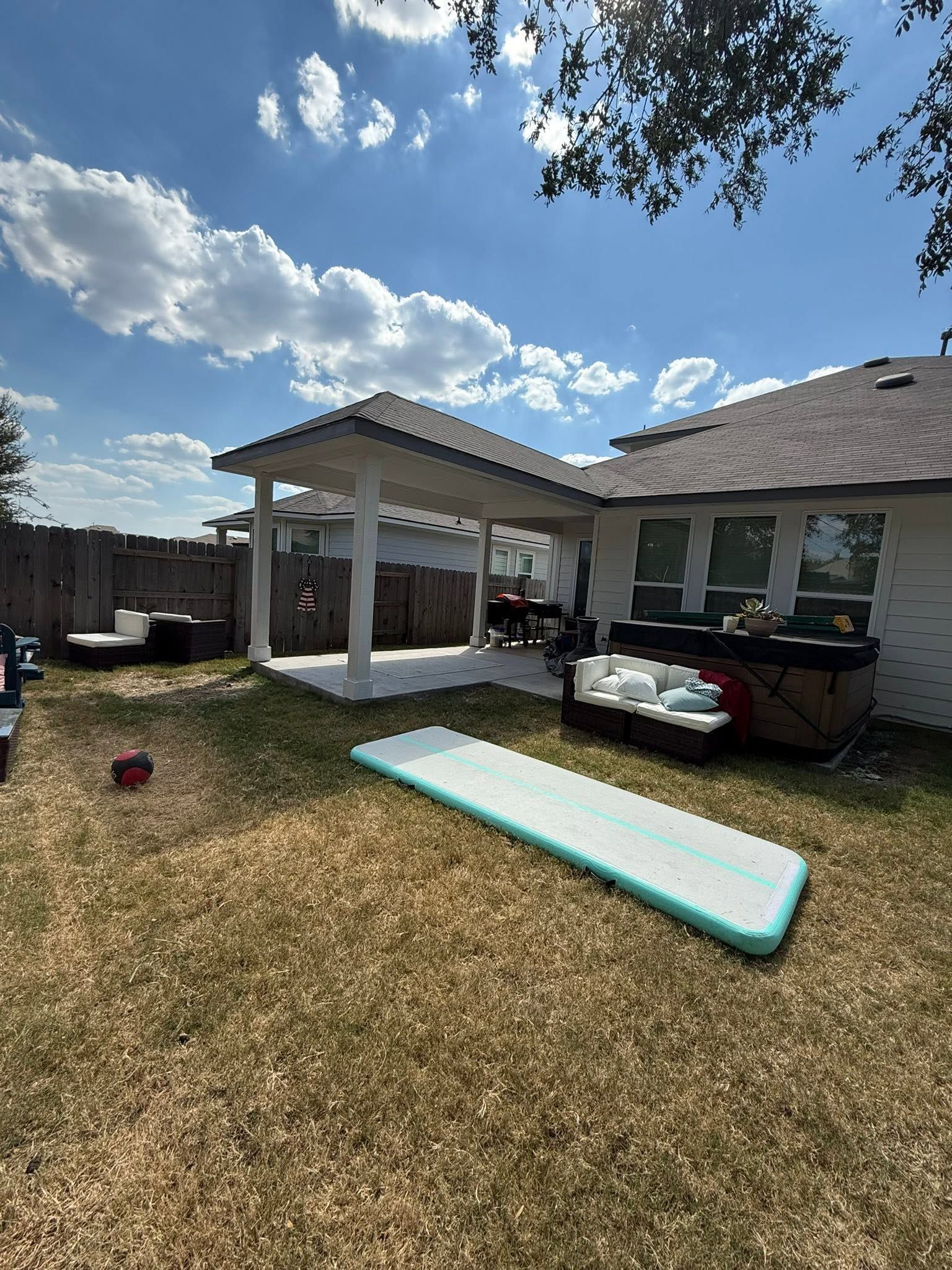 Backyard patio with covered seating area, a hot tub, and a turquoise pool float on the grass.