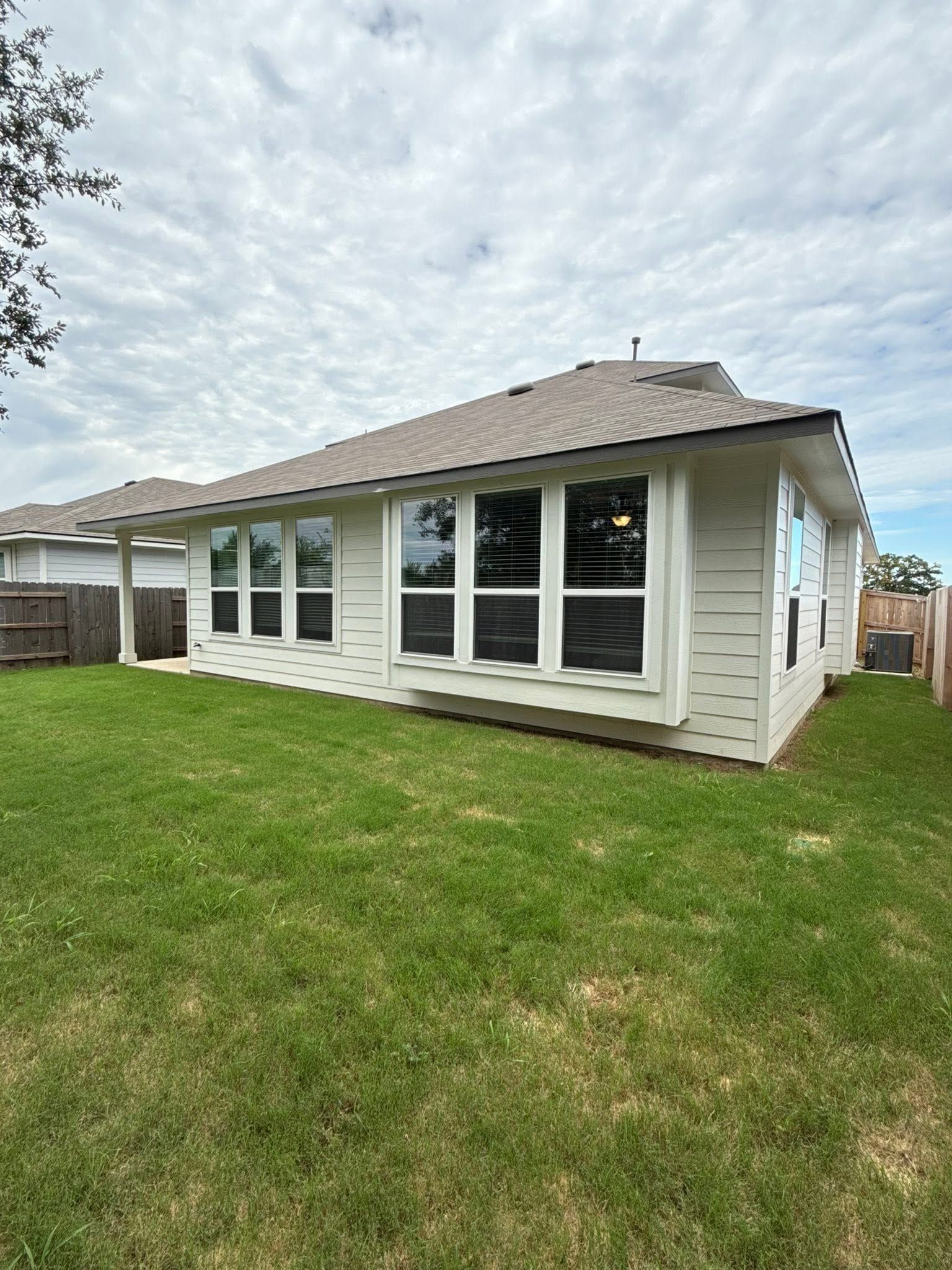 White single-story house with large front windows and a grassy yard under cloudy sky