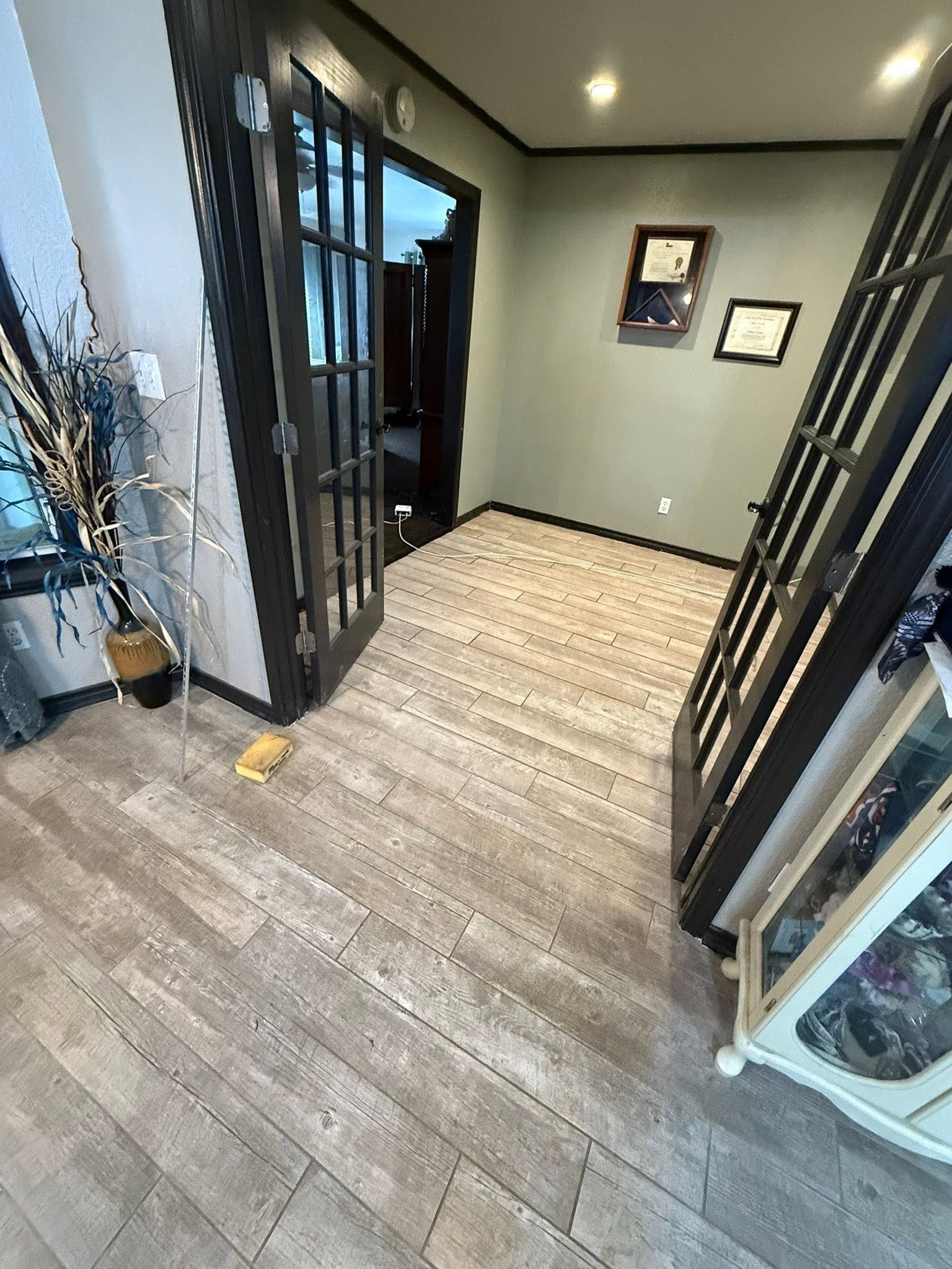 Narrow entry hallway with gray walls, wood-look tile floor, black door frames, and wall decor.