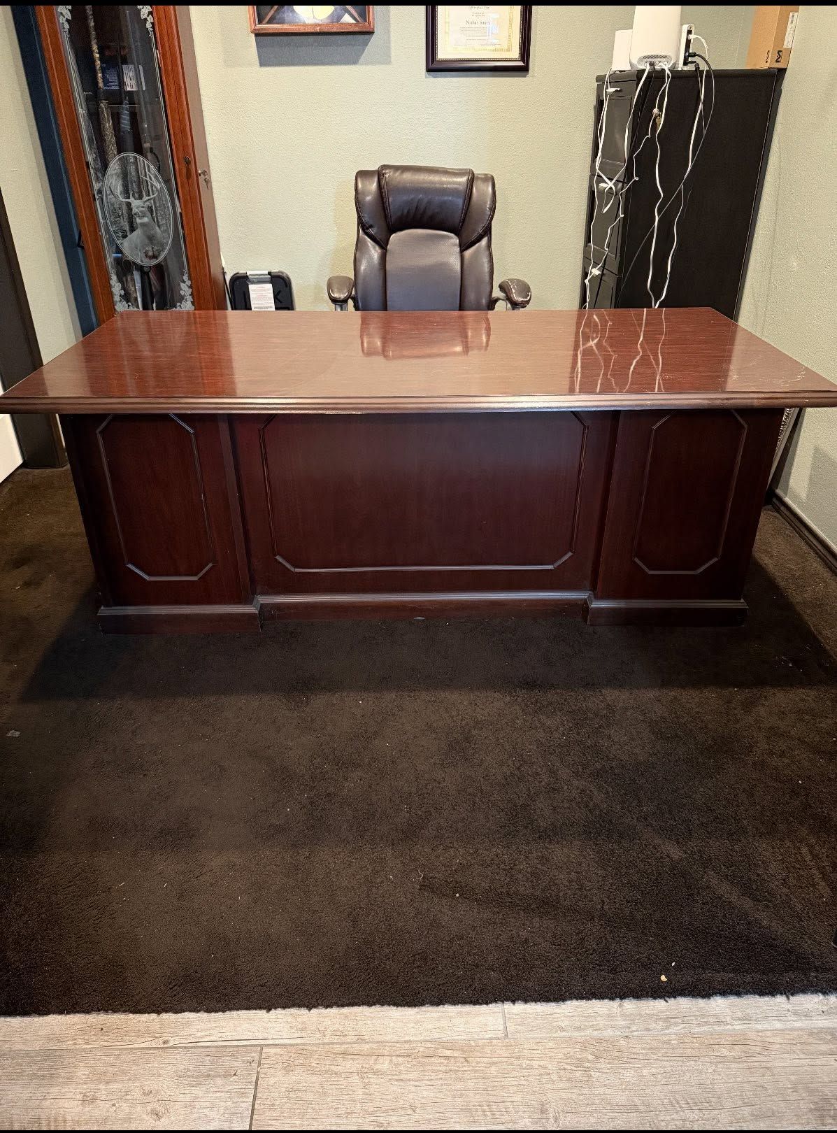 Office desk with a brown chair behind it on a dark carpeted floor.