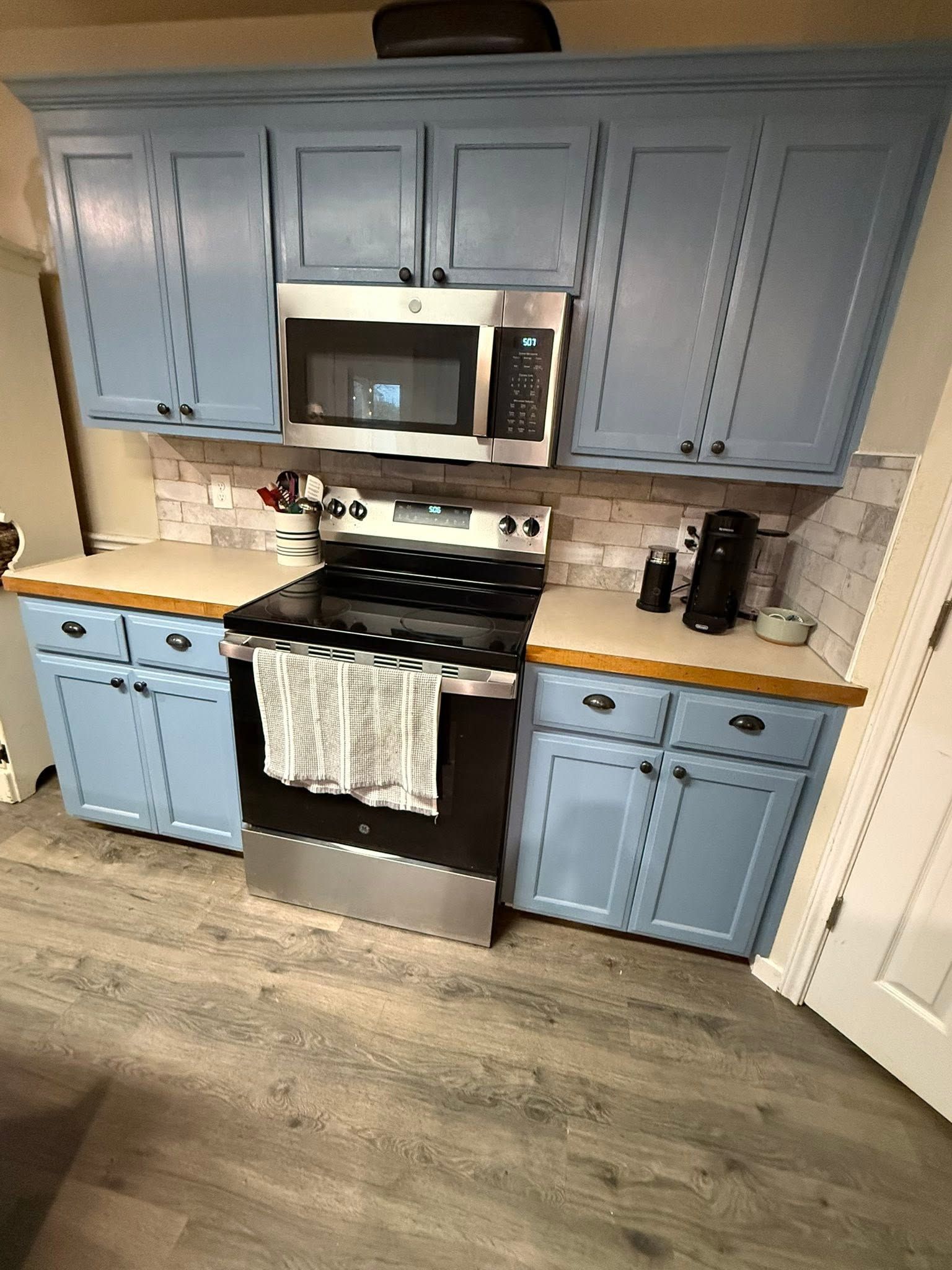 Blue kitchen with stainless steel stove and microwave, white countertops, and wood-look flooring