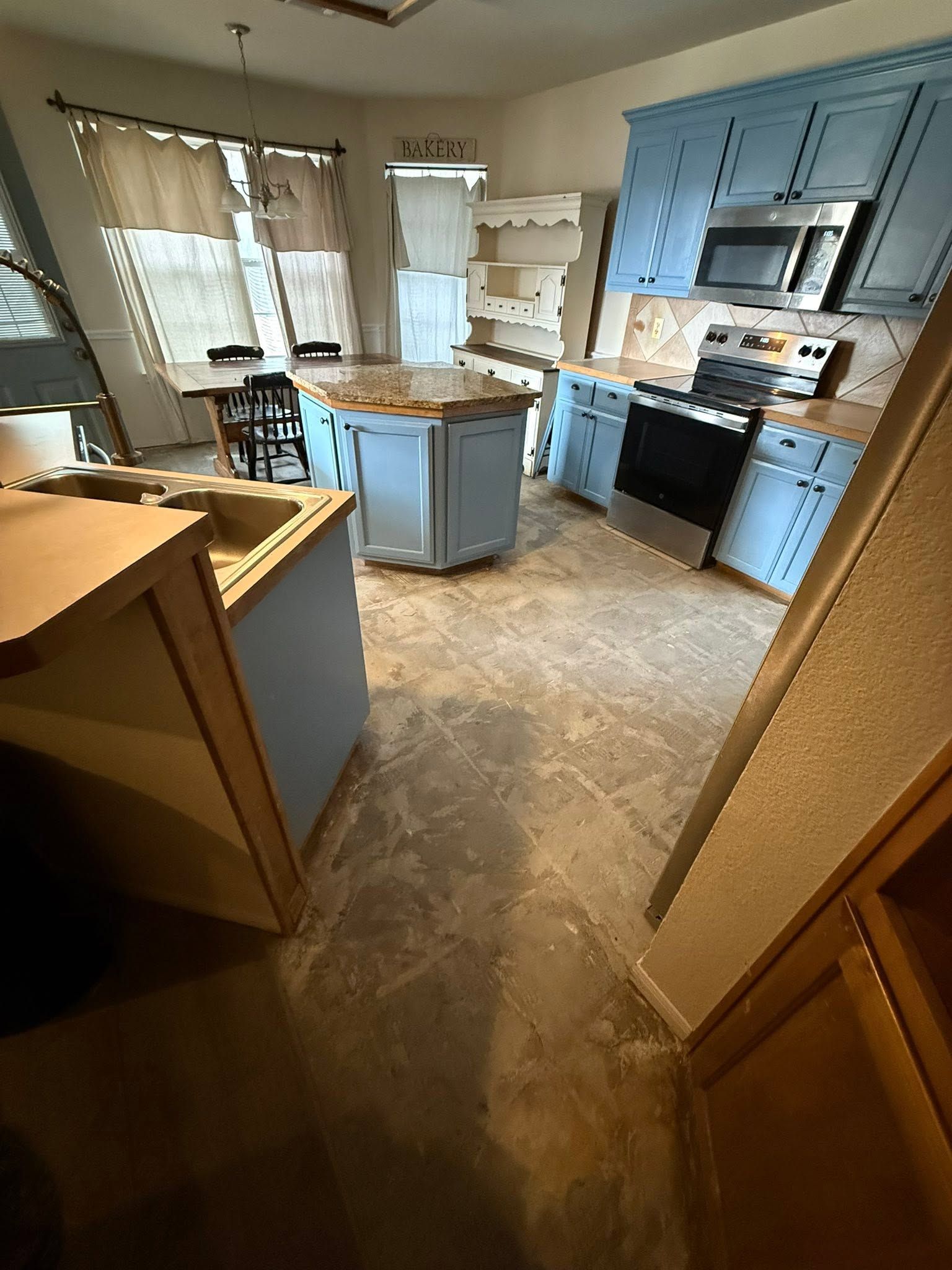 Empty kitchen with blue cabinets, island, stove, microwave, and bright windows.