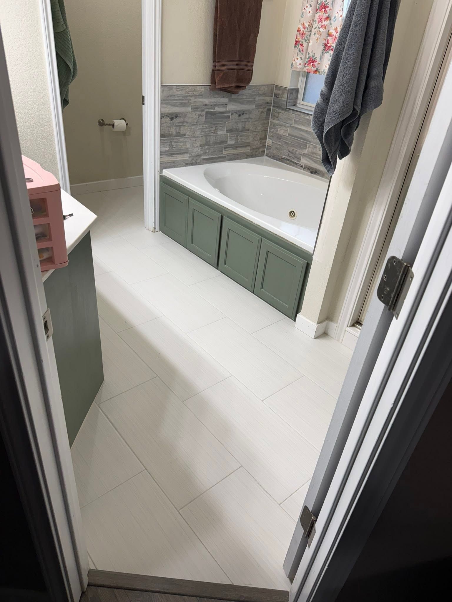 Bathroom hallway view with white tile floor, green tub, and gray tiled shower area.