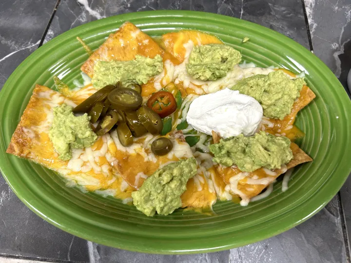 Green plate of nachos topped with guacamole, sour cream, jalapeños, and melted cheese