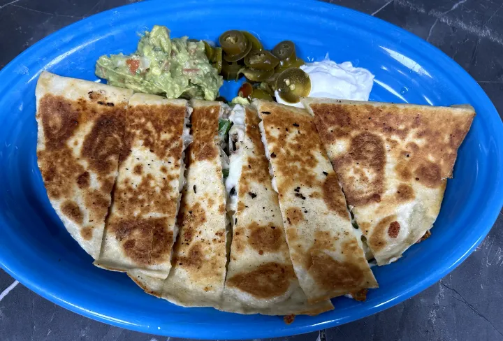 Blue plate with folded quesadilla, guacamole, sour cream, and jalapeños