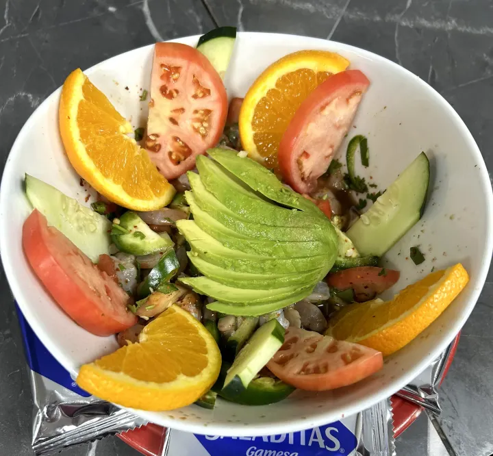 Citrus and avocado salad in a white bowl, topped with orange and tomato slices
