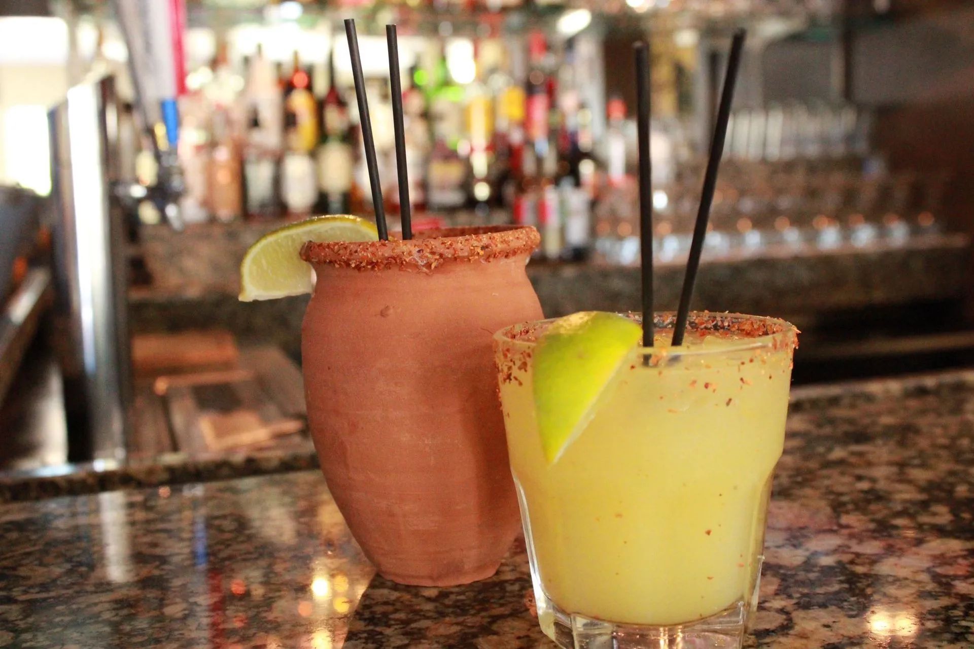 Two colorful cocktails with lime garnishes and straws on a bar counter