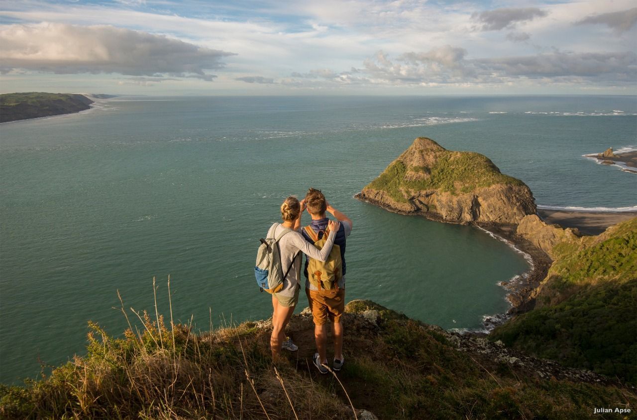 Um homem e uma mulher estão no topo de um penhasco com vista para o oceano.
