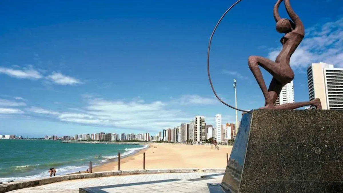 Uma estátua de uma mulher segurando um bambolê em frente a uma praia.